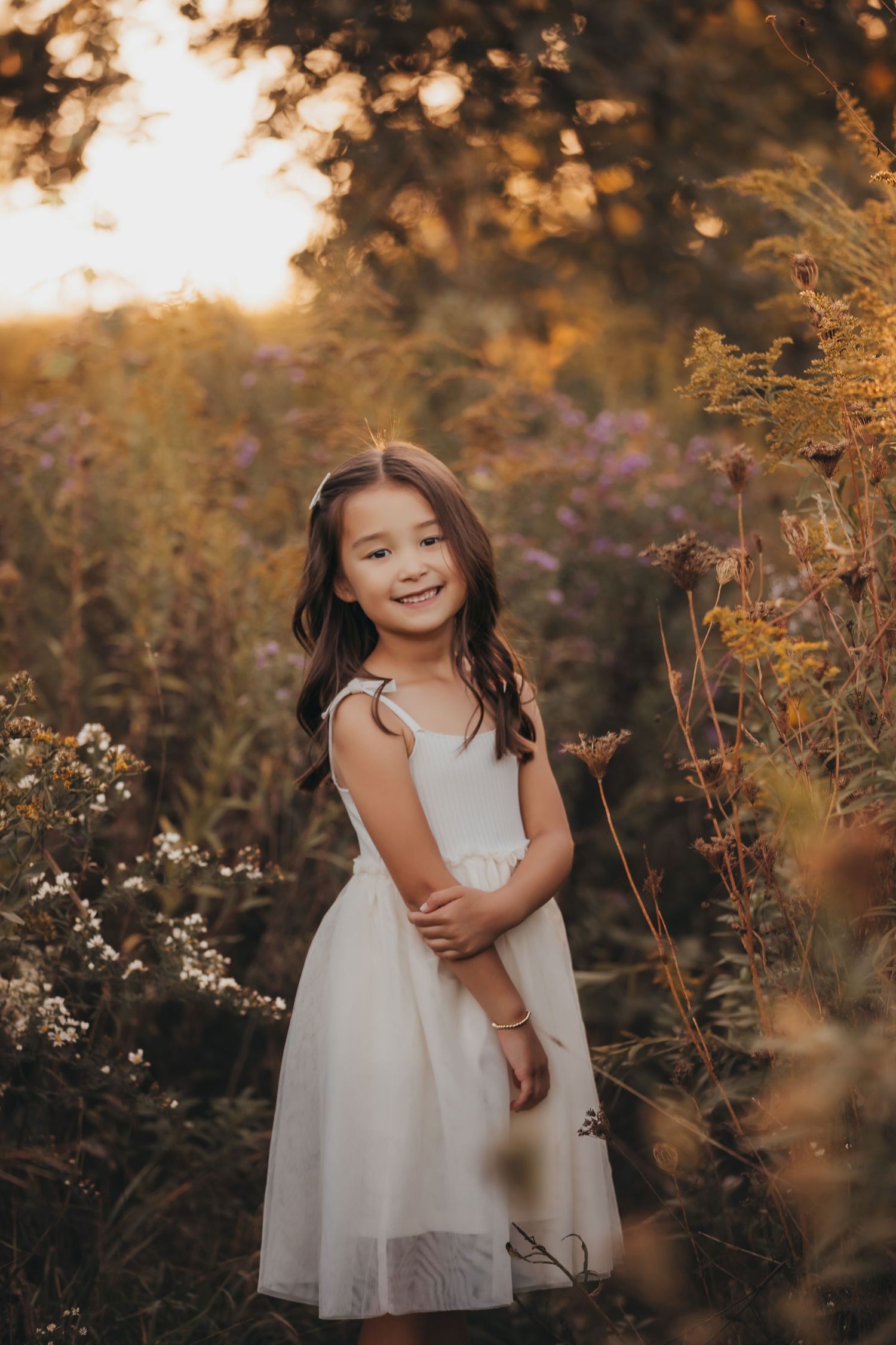 Young girl in white dress smiling in a golden hour wildflower field.