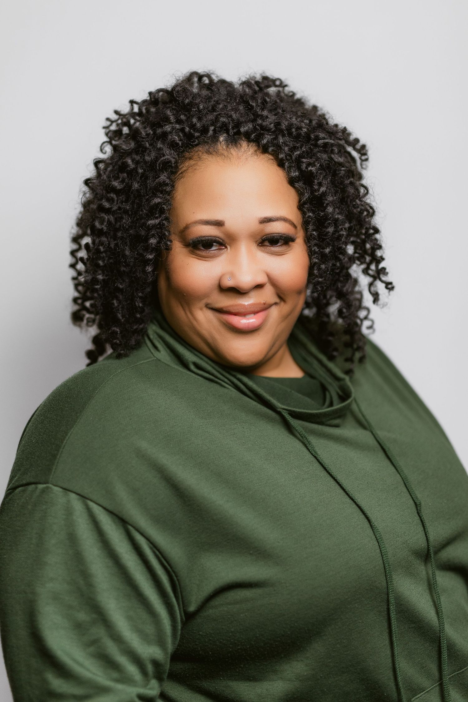 Professional headshot of person in olive green top against grey background.