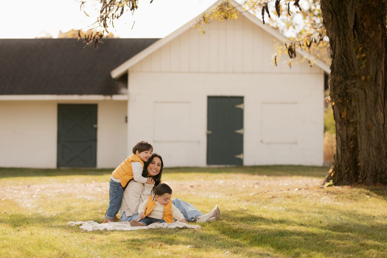 A family relaxes on a blanket near a white barn on a sunny day.