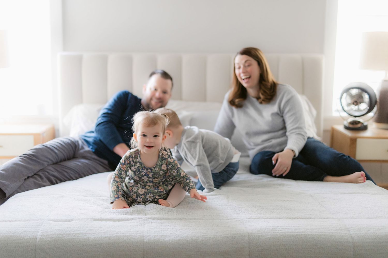 Family relaxing together on a white bed in sunny bedroom while moving into new home.