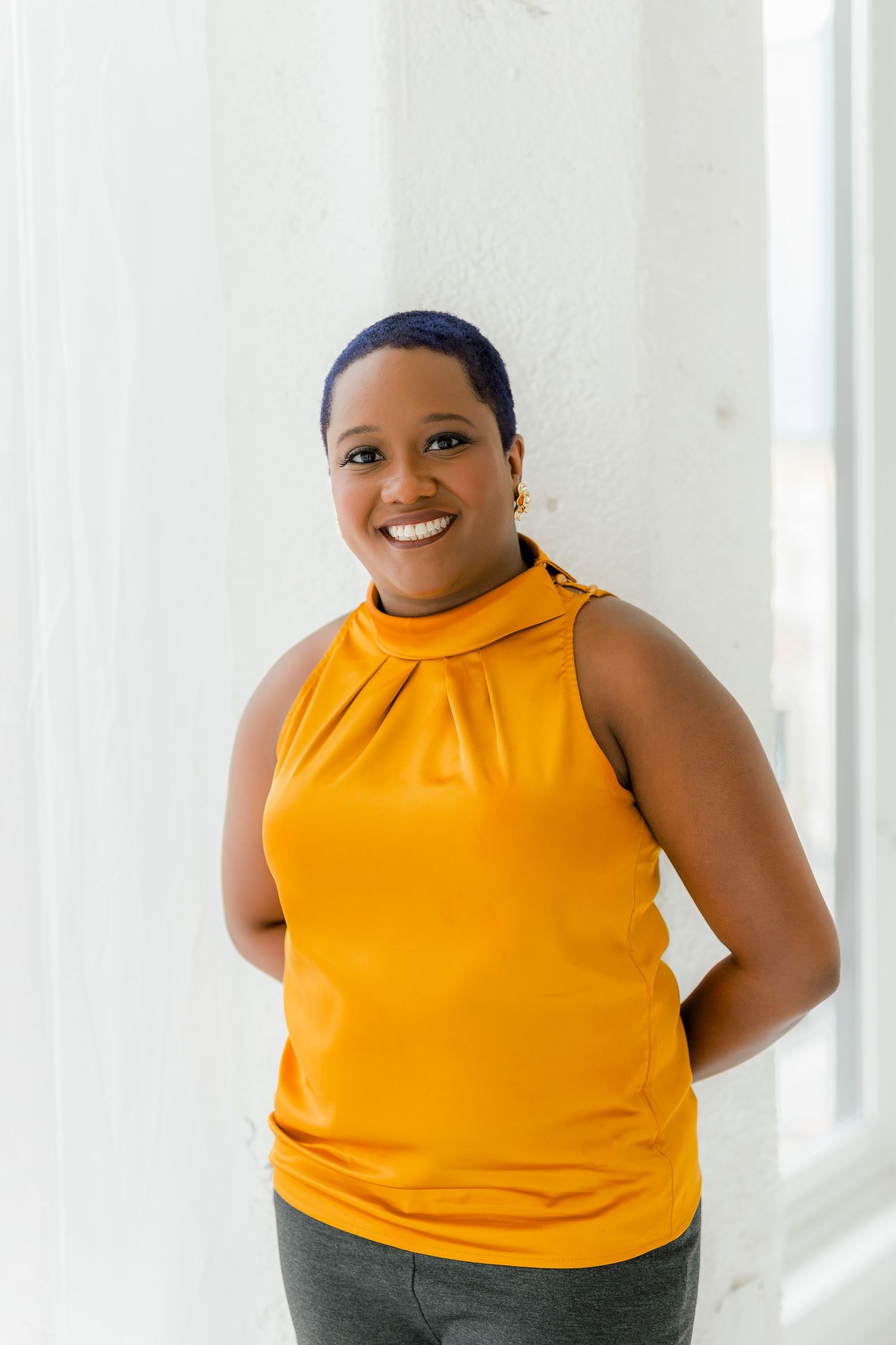 Professional portrait in bright yellow sleeveless top against white wall.
