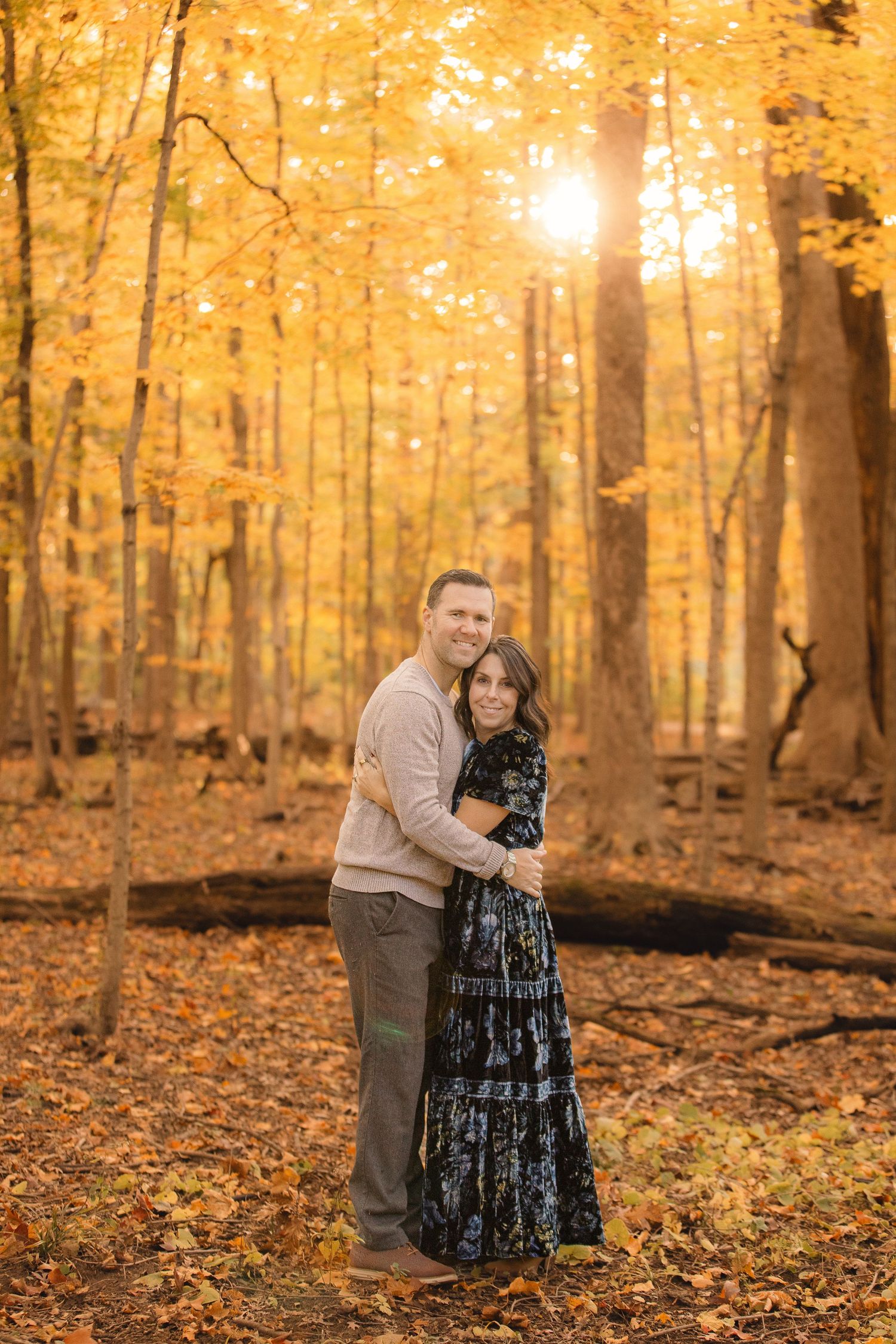 Couple embracing in sunlit autumn forest with golden leaves and warm lighting.