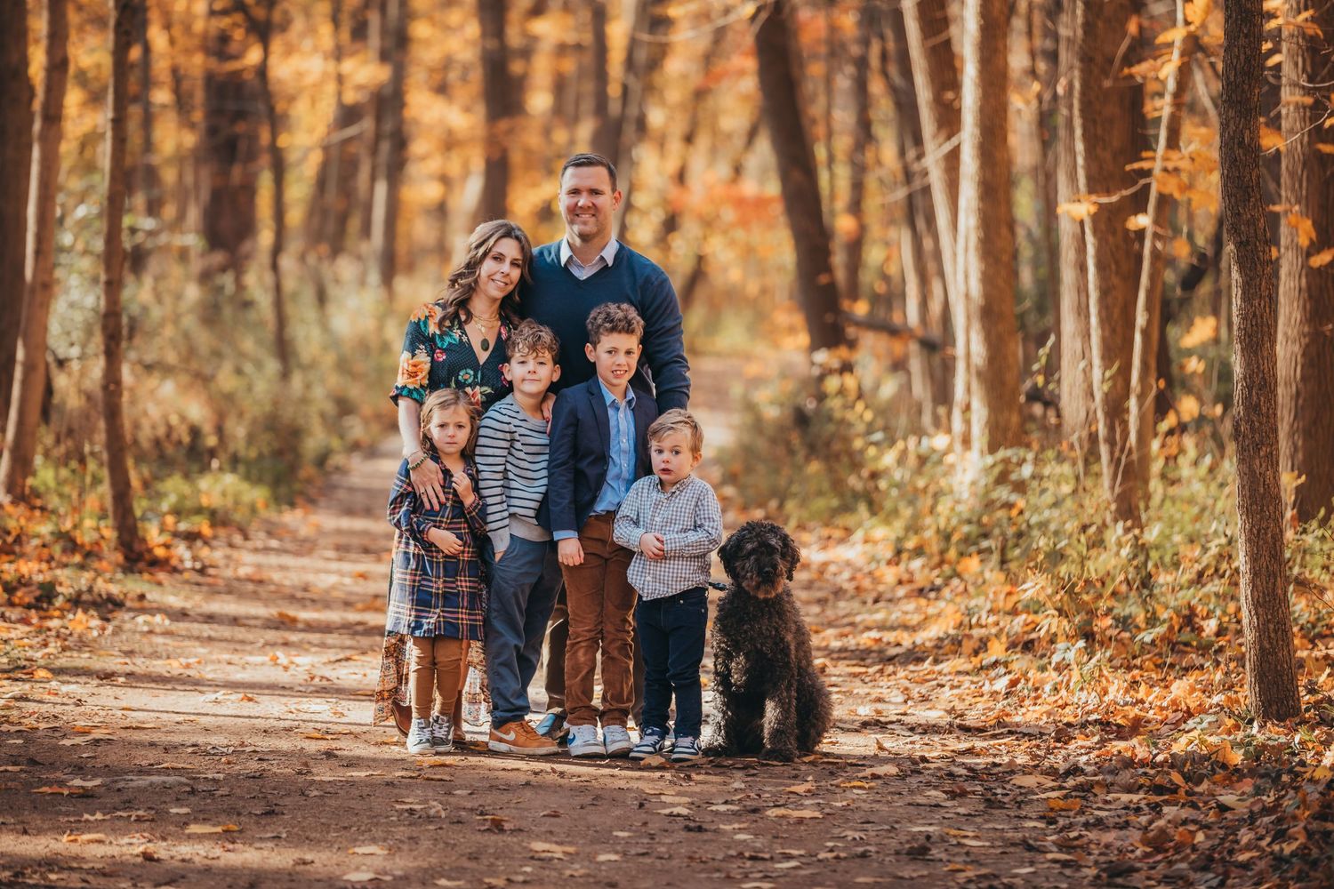 Family and black dog walking together on autumn forest trail with golden leaves.