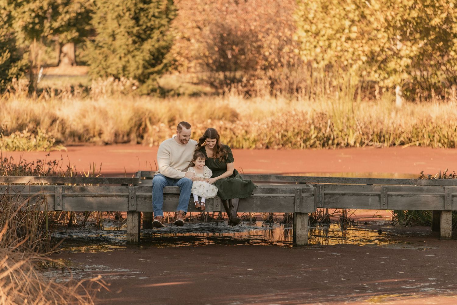 Couple sitting on wooden bench in park during golden sunset with autumn colors surrounding them.