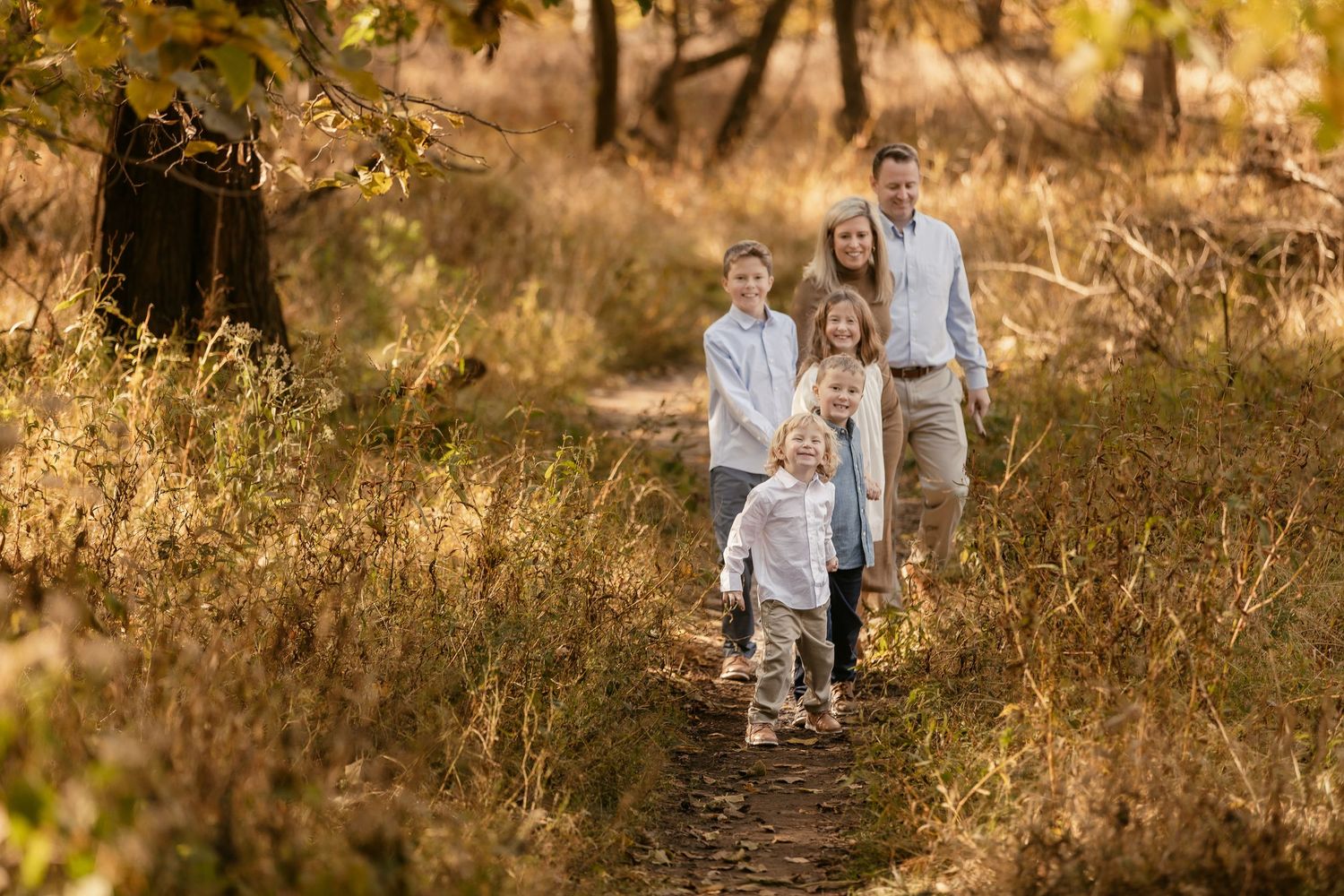 A family walks together on a sunlit trail through golden autumn foliage.
