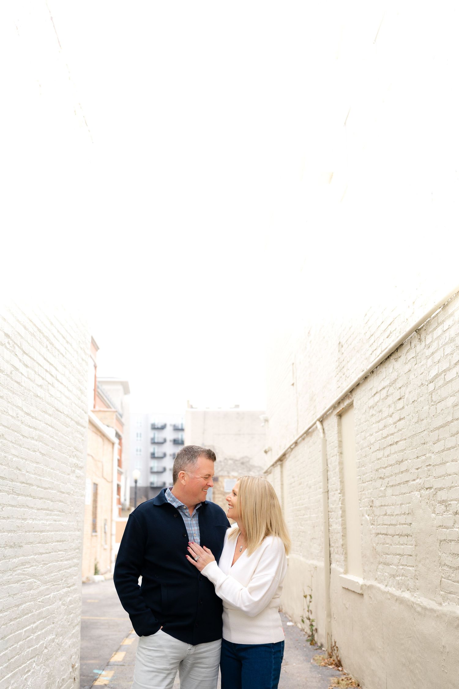 Couple shares intimate moments against white brick wall background.