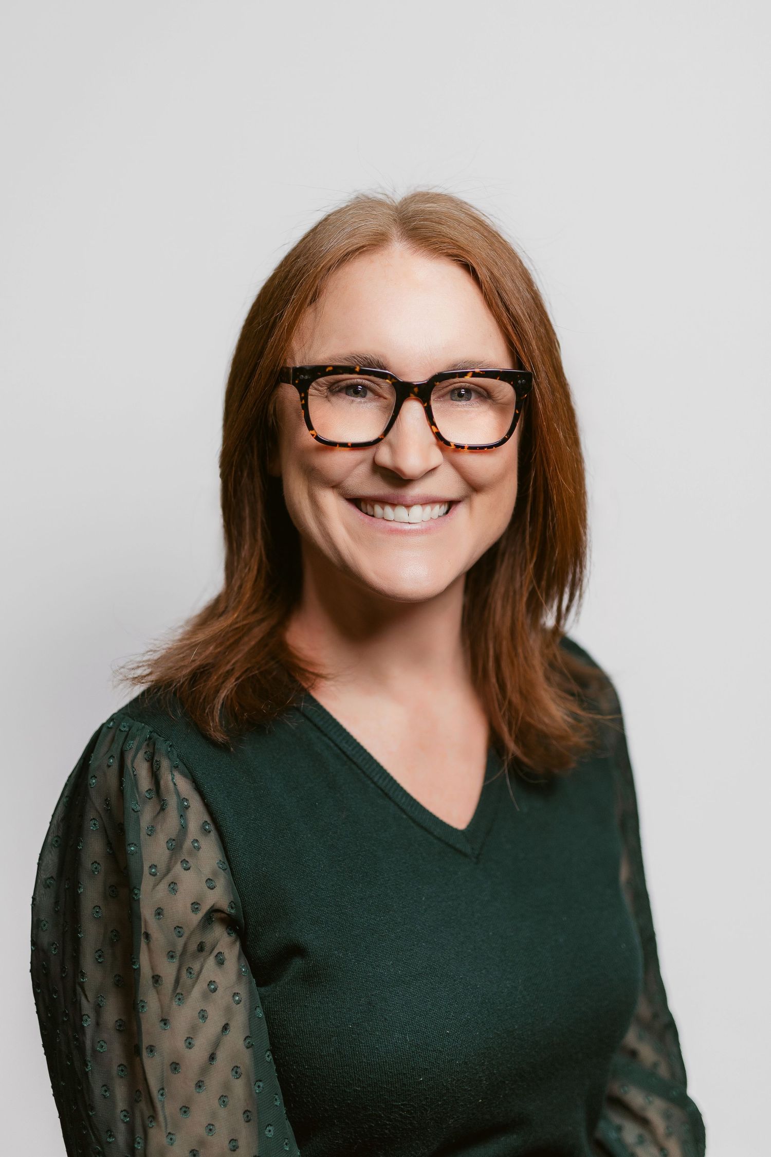 Professional headshots of person wearing glasses and dark v-neck top with sheer sleeves.
