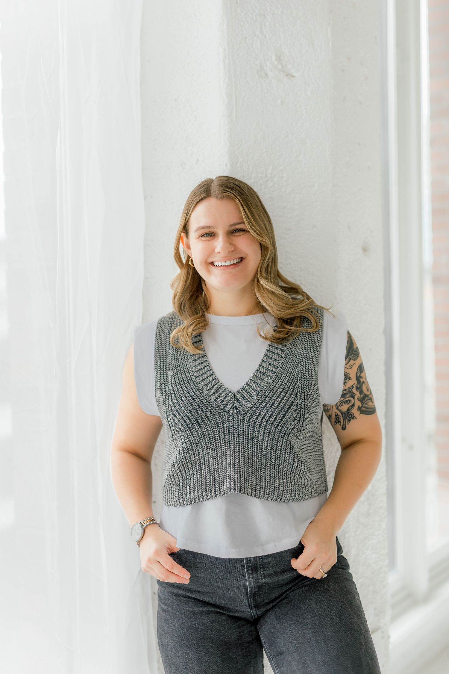 Casual portrait against white wall wearing gray knit vest and white t-shirt.