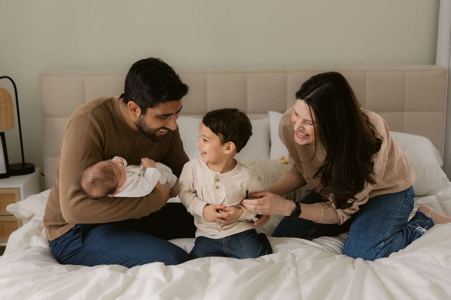 Family members lying together on a white bed sharing tender moments and cuddles in a lifestyle photography series.