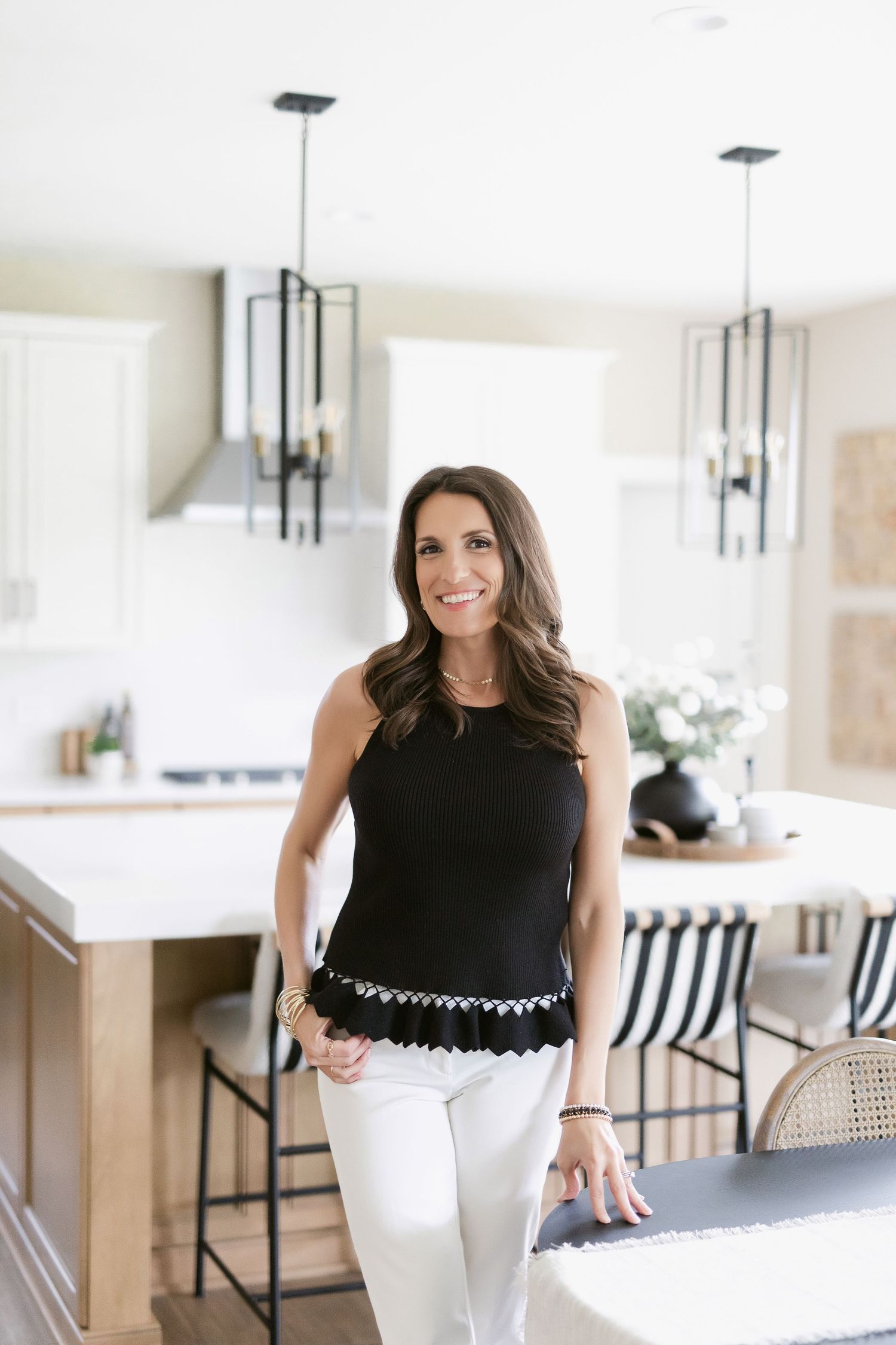 Professional in black top and white pants stands casually in modern kitchen setting.