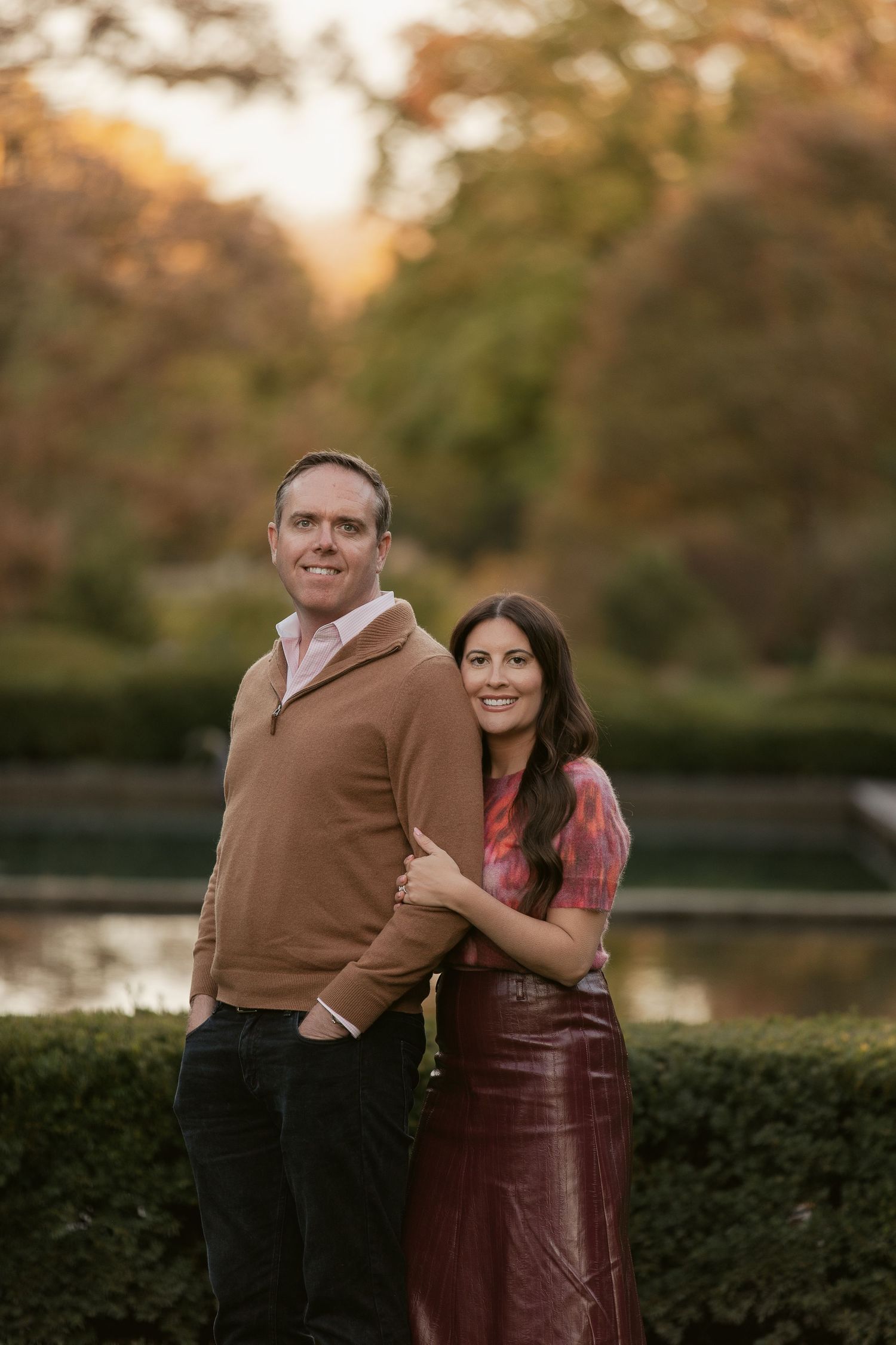 A couple poses together in an elegant garden setting during golden hour.