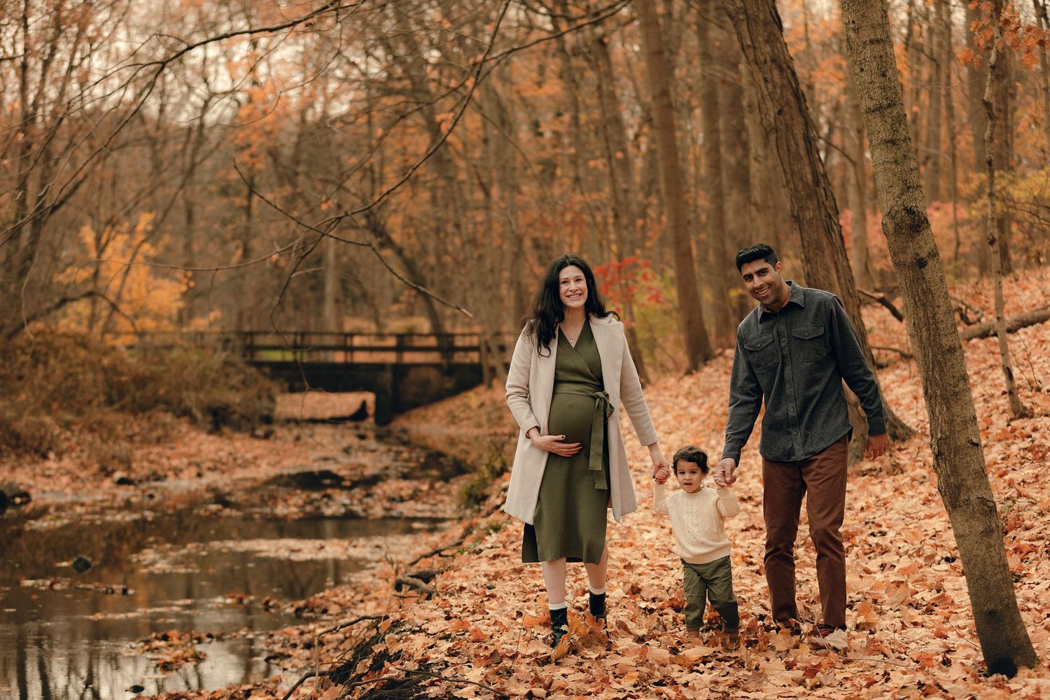 Family enjoying autumn day together on wooden bridge over stream.