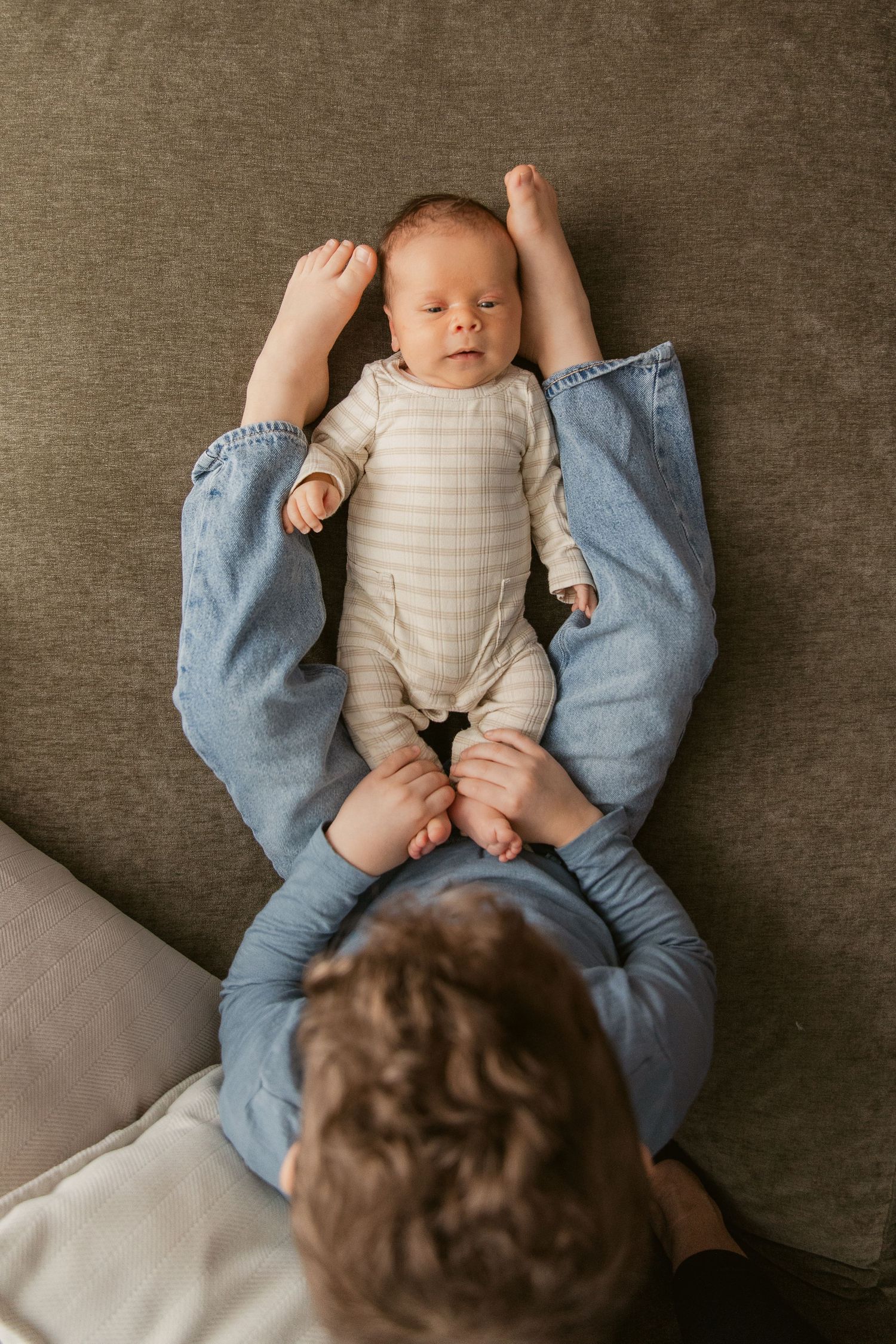 Overhead view of siblings bonding on a gray couch, one wearing blue denim.