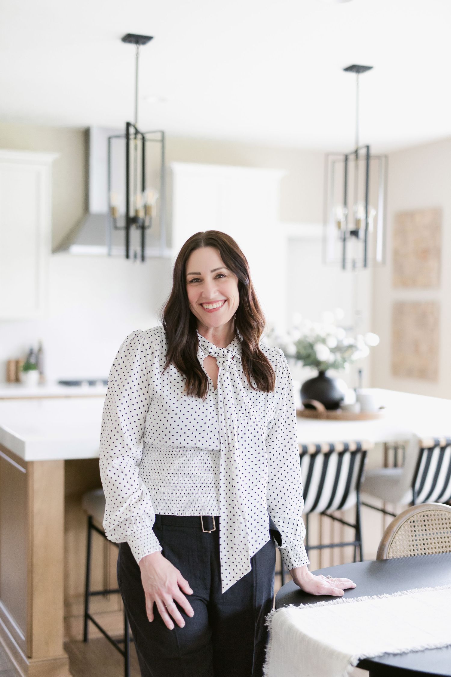Professional in polka dot blouse smiles while standing at counter in contemporary kitchen.