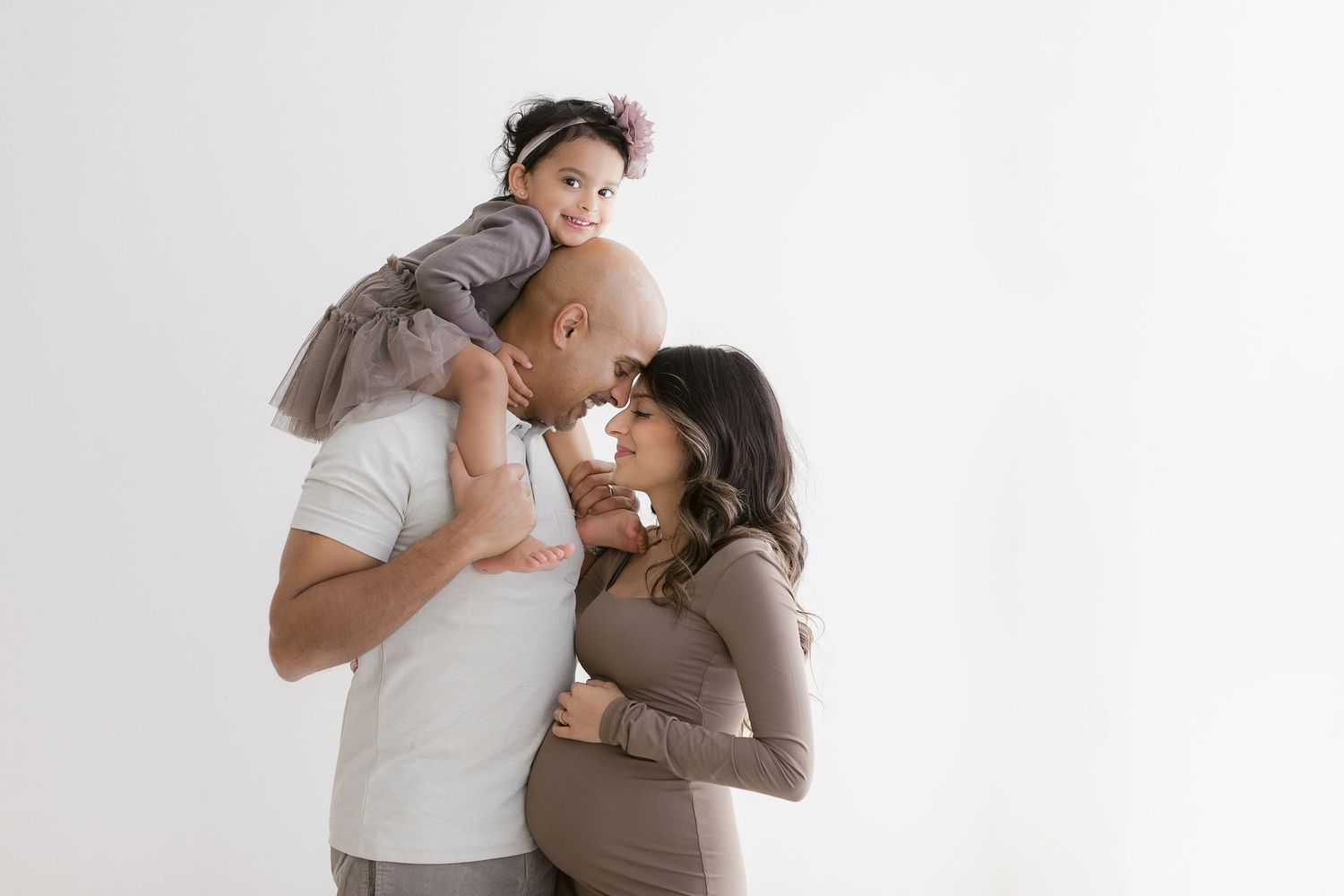 A family in neutral-toned clothing laughs together against a white backdrop during a minimalist studio portrait session.
