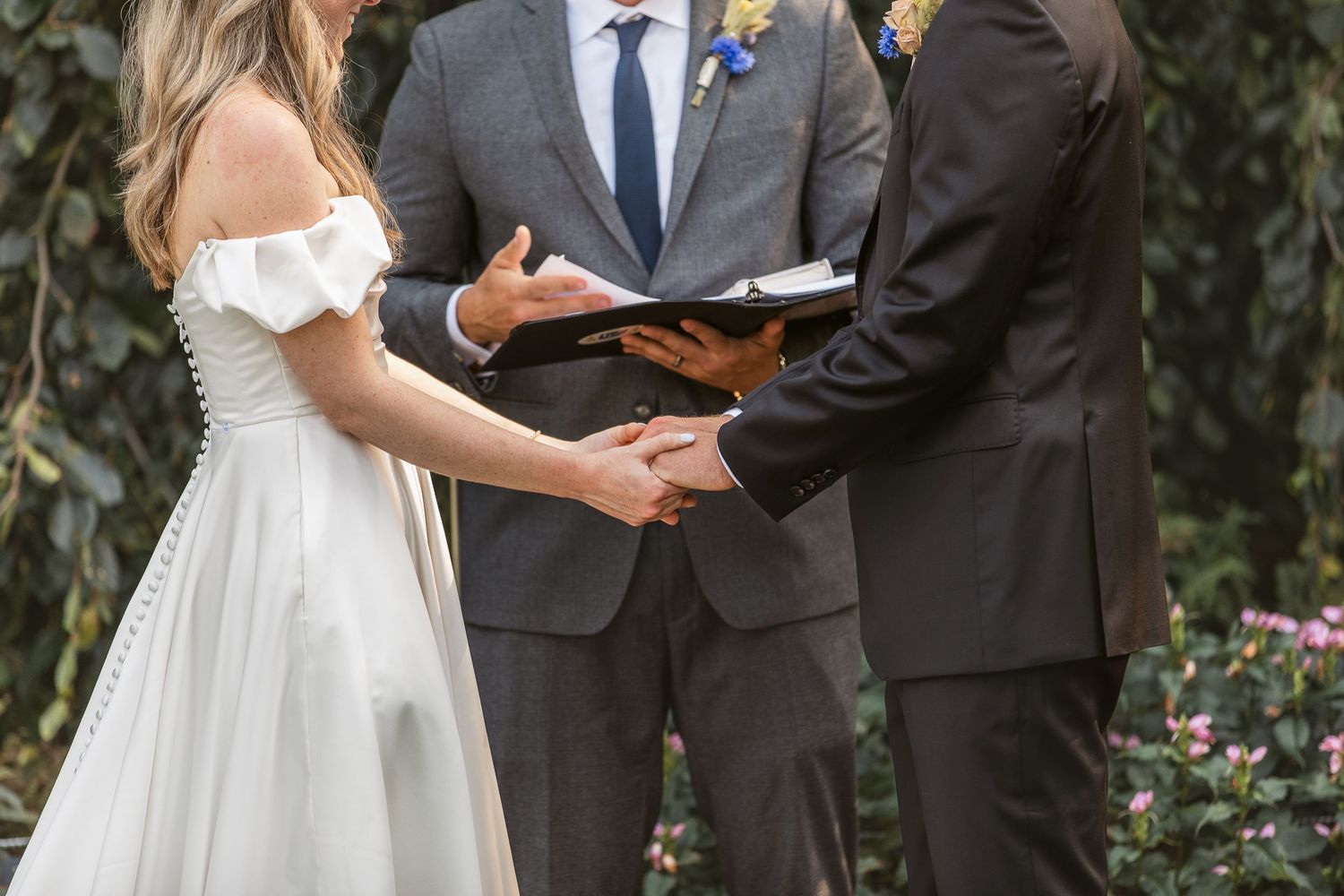 A couple exchanges vows during an outdoor garden wedding ceremony with lush greenery in the background.
