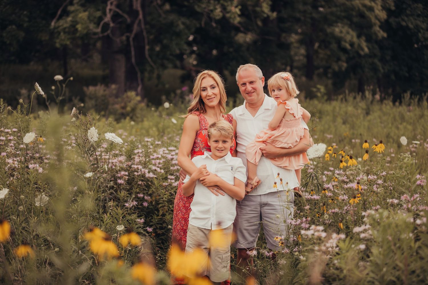 A family stands together in a wildflower meadow on a summer day surrounded by colorful blooms.