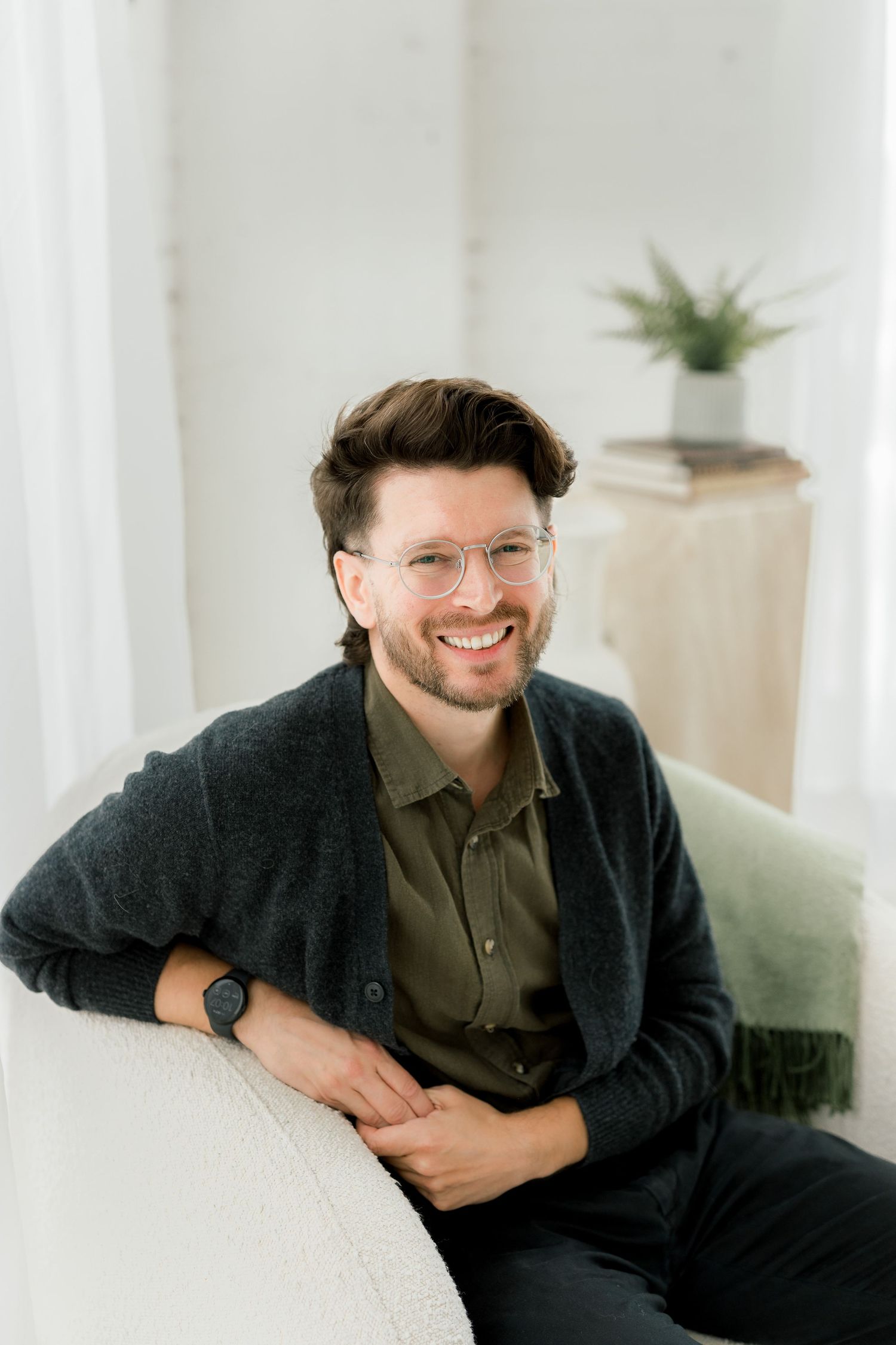 Professional portrait in a bright interior space wearing glasses, dark cardigan and olive shirt.