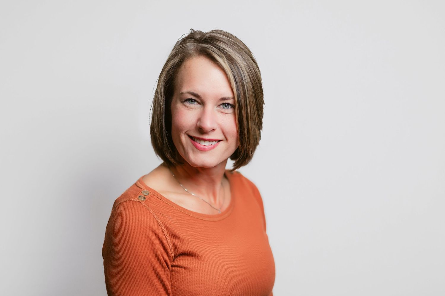Professional headshots of person in orange top with short hair against light background.