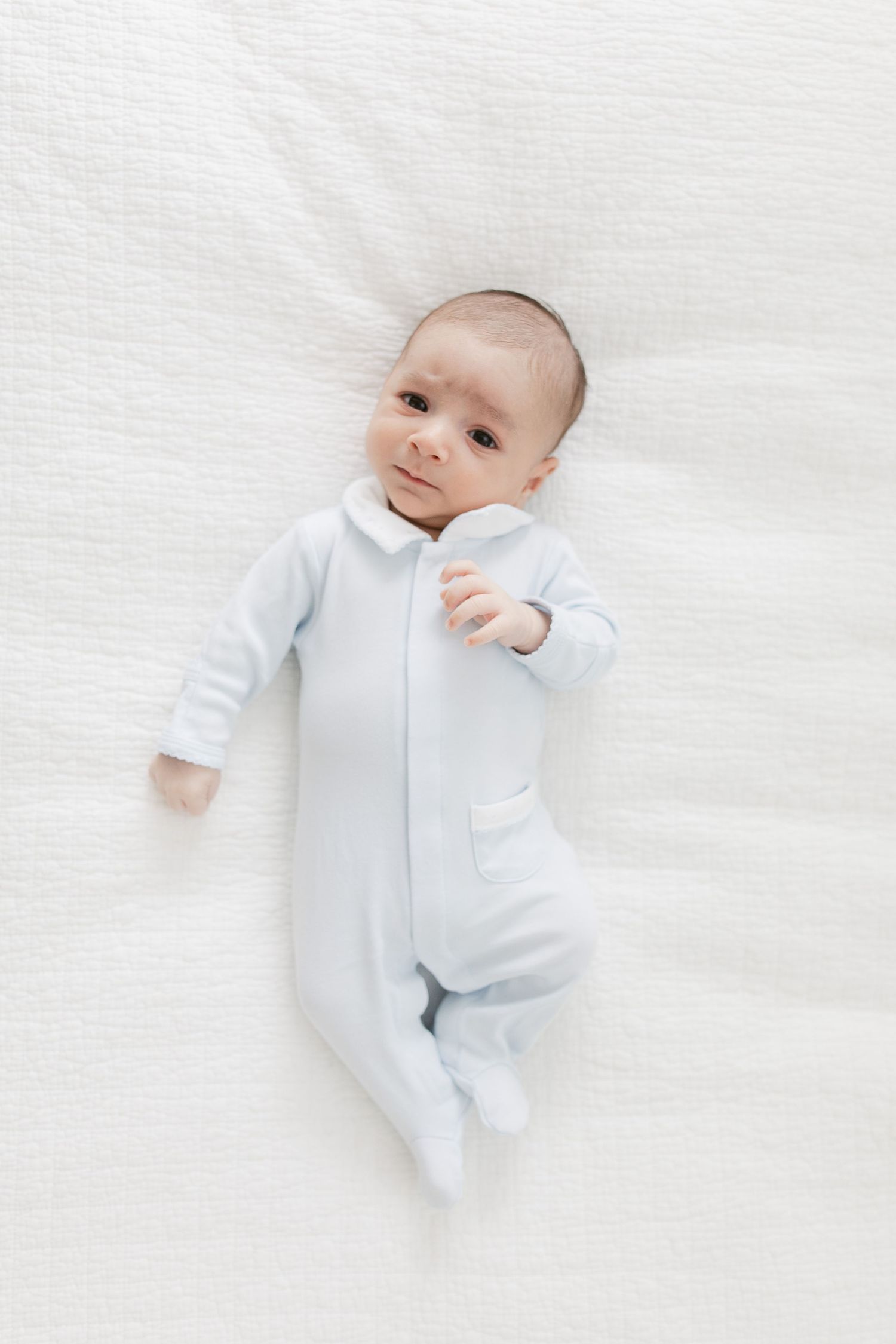 Sweet baby in light blue sleeper lying on white blanket in three different poses.