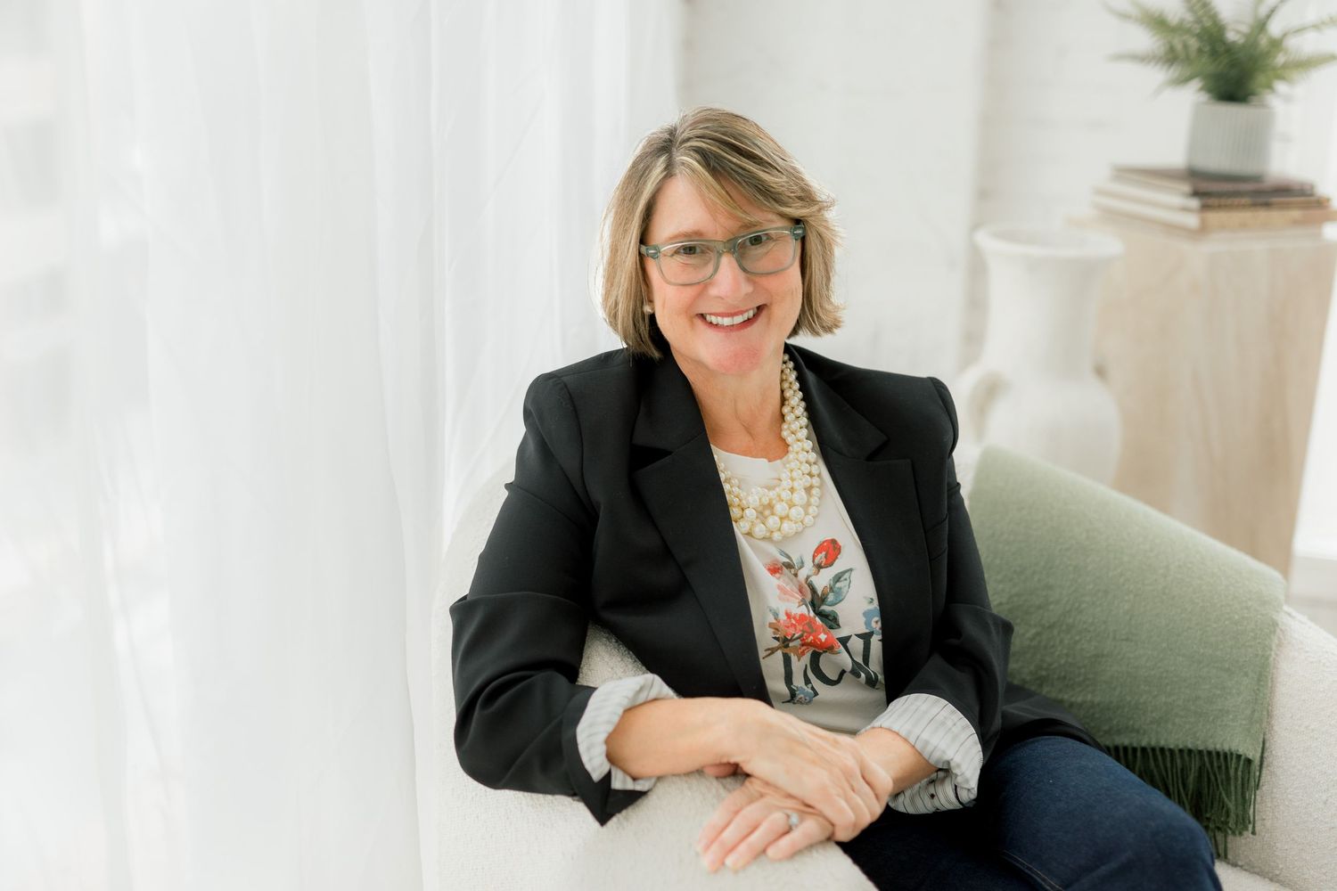 Person in black blazer sits comfortably on green furniture.