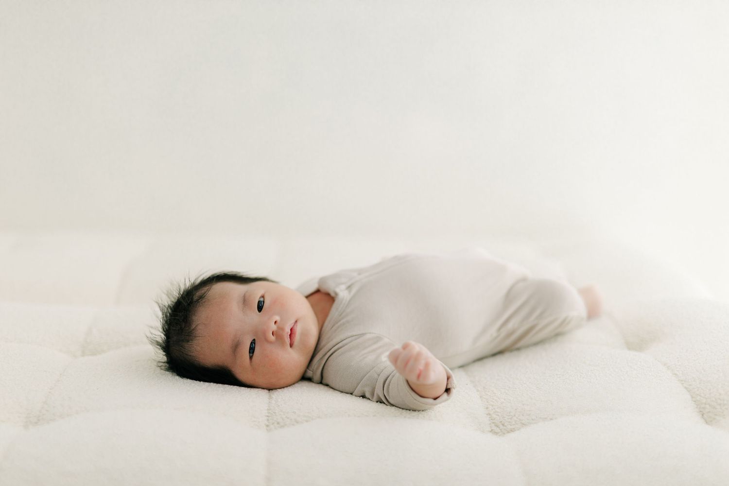 Peaceful newborn in white clothing lying on soft white bedding.