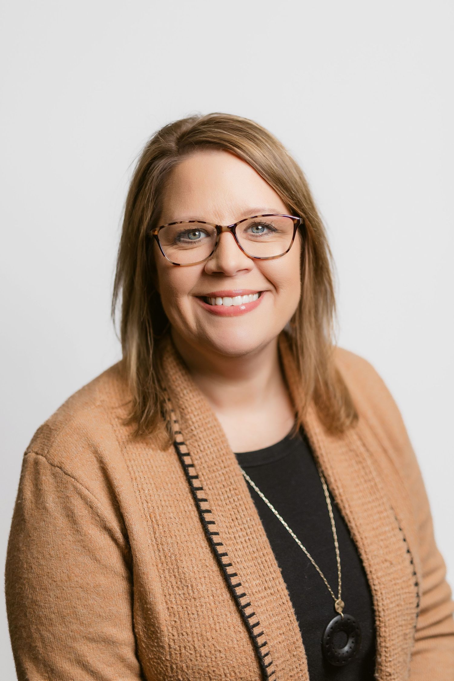 Professional headshots of a person wearing glasses and tan cardigan against white background.