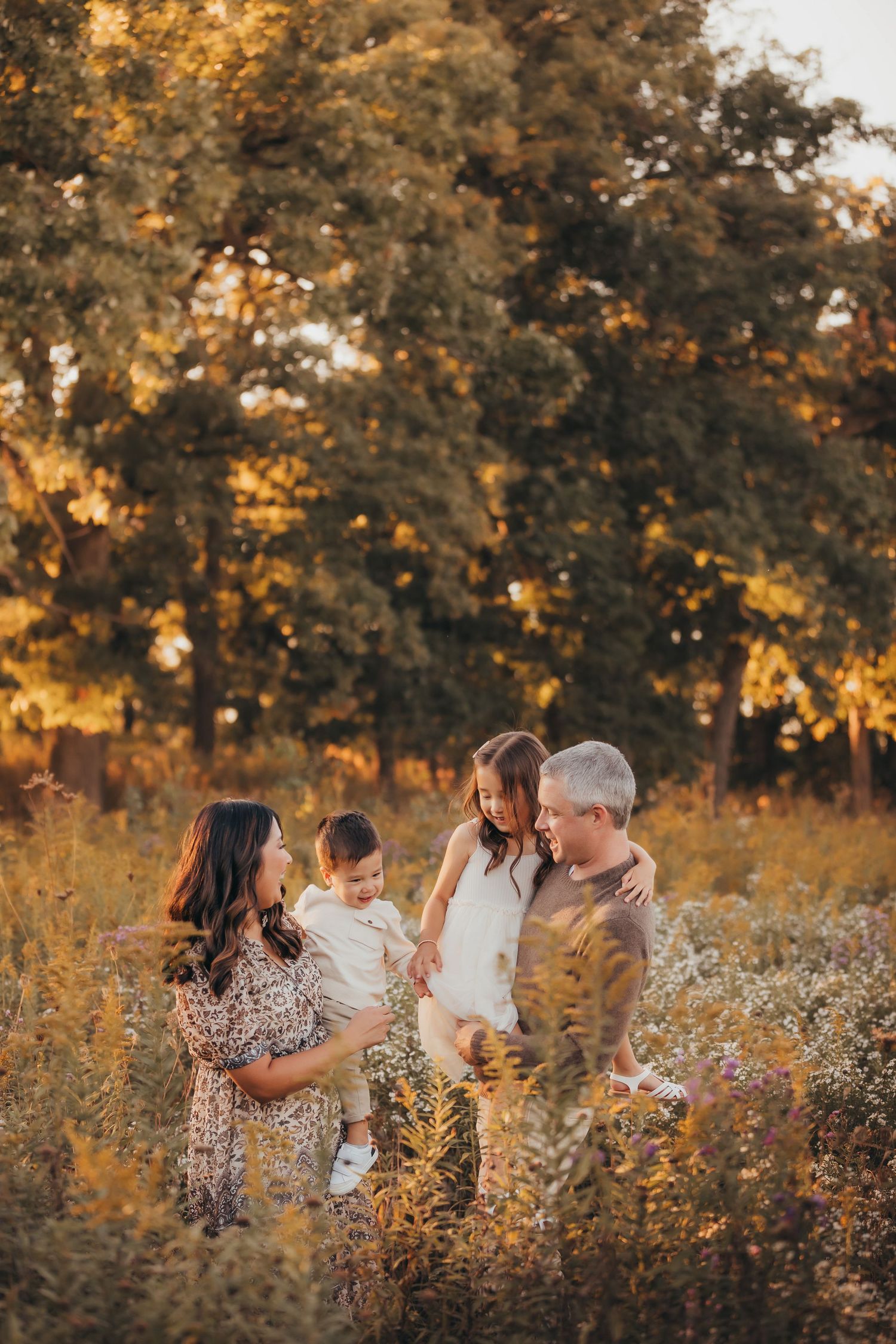 Family of four enjoying golden hour in a wildflower meadow, with tall trees in the warm sunset background.