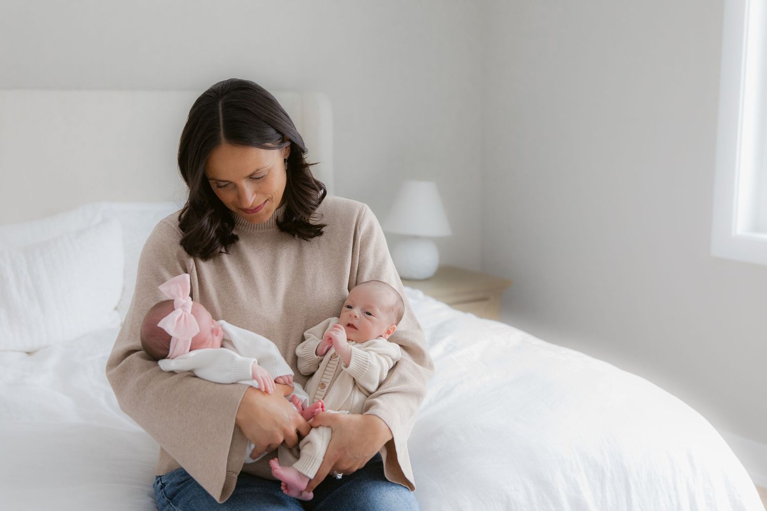 A tender moment of parent and newborn baby resting together on white bedding in a bright, airy room.