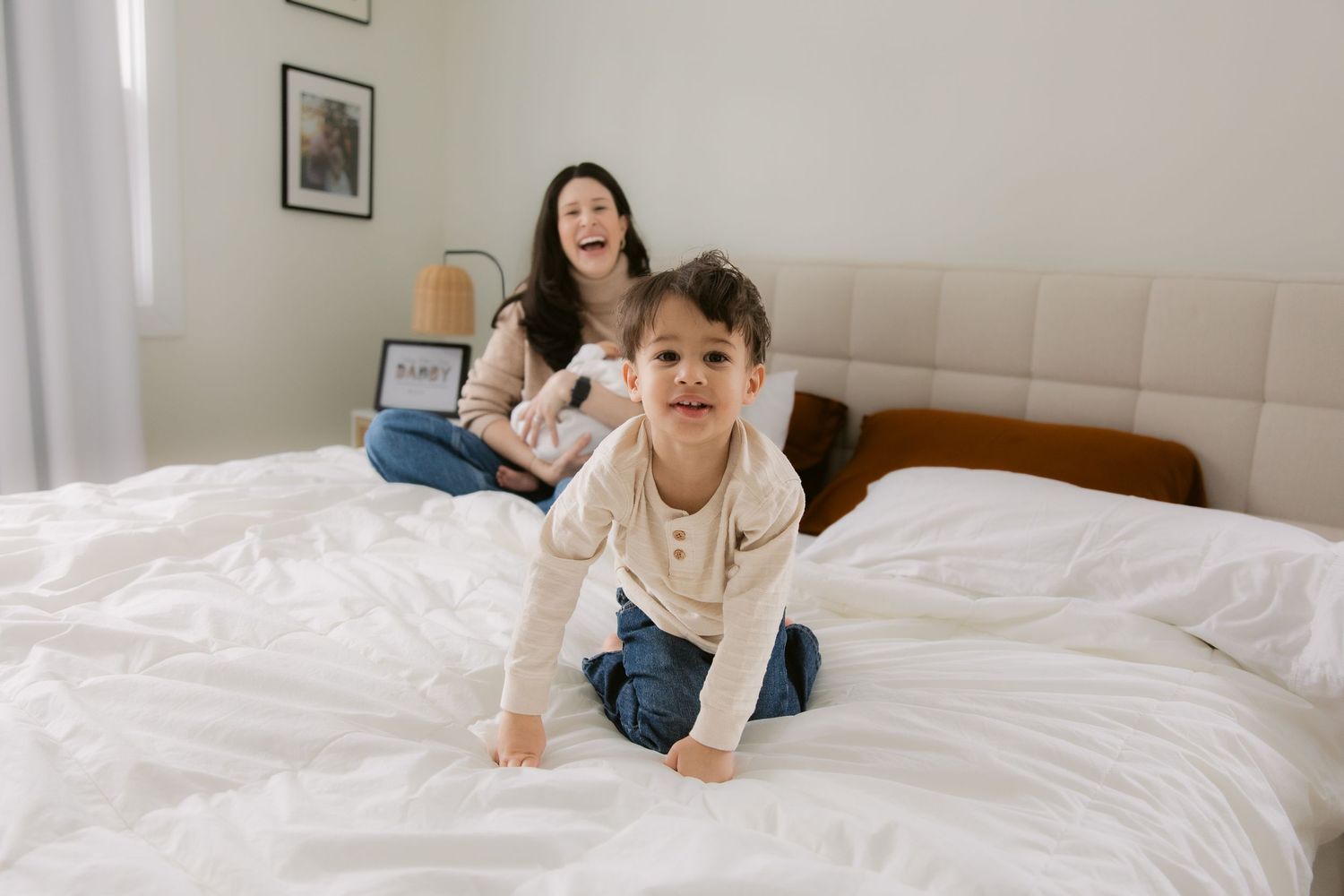 Child in white sweater lying on a cozy white bed with natural light streaming through windows.