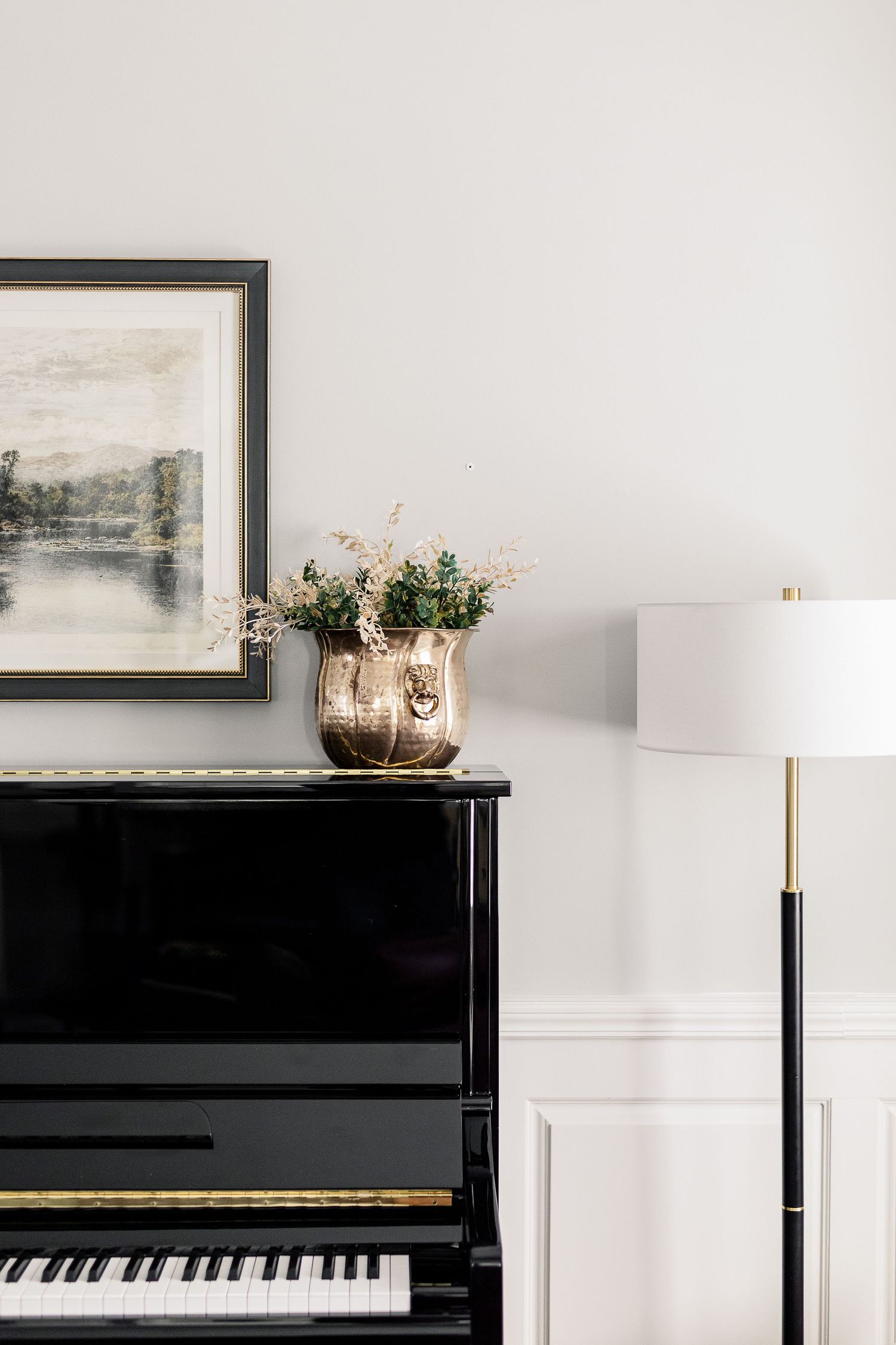 Elegant piano display with framed artwork and floral arrangement on a black upright piano against white walls.
