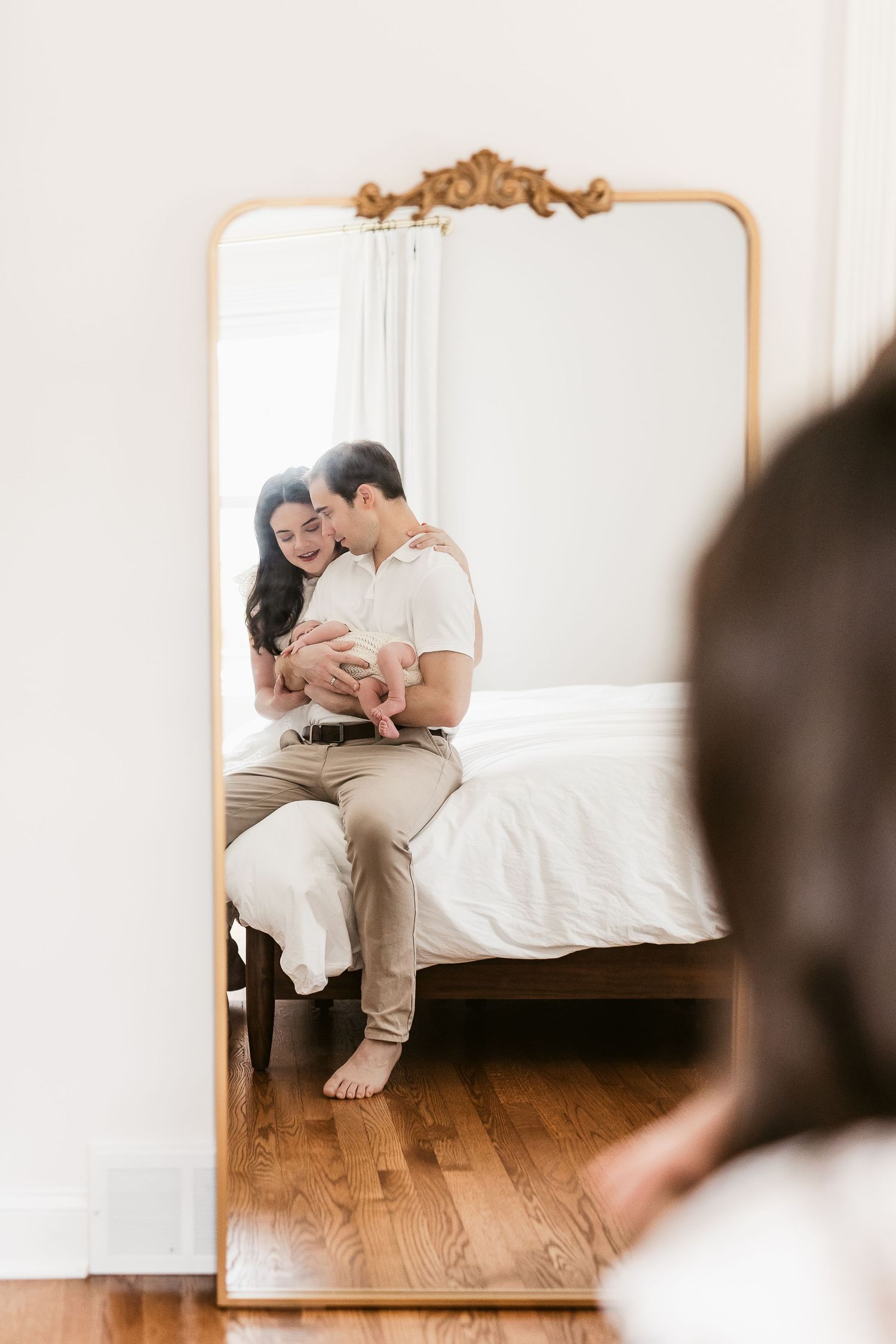 Intimate moment captured in a bright white bedroom with ornate gold-framed mirror.