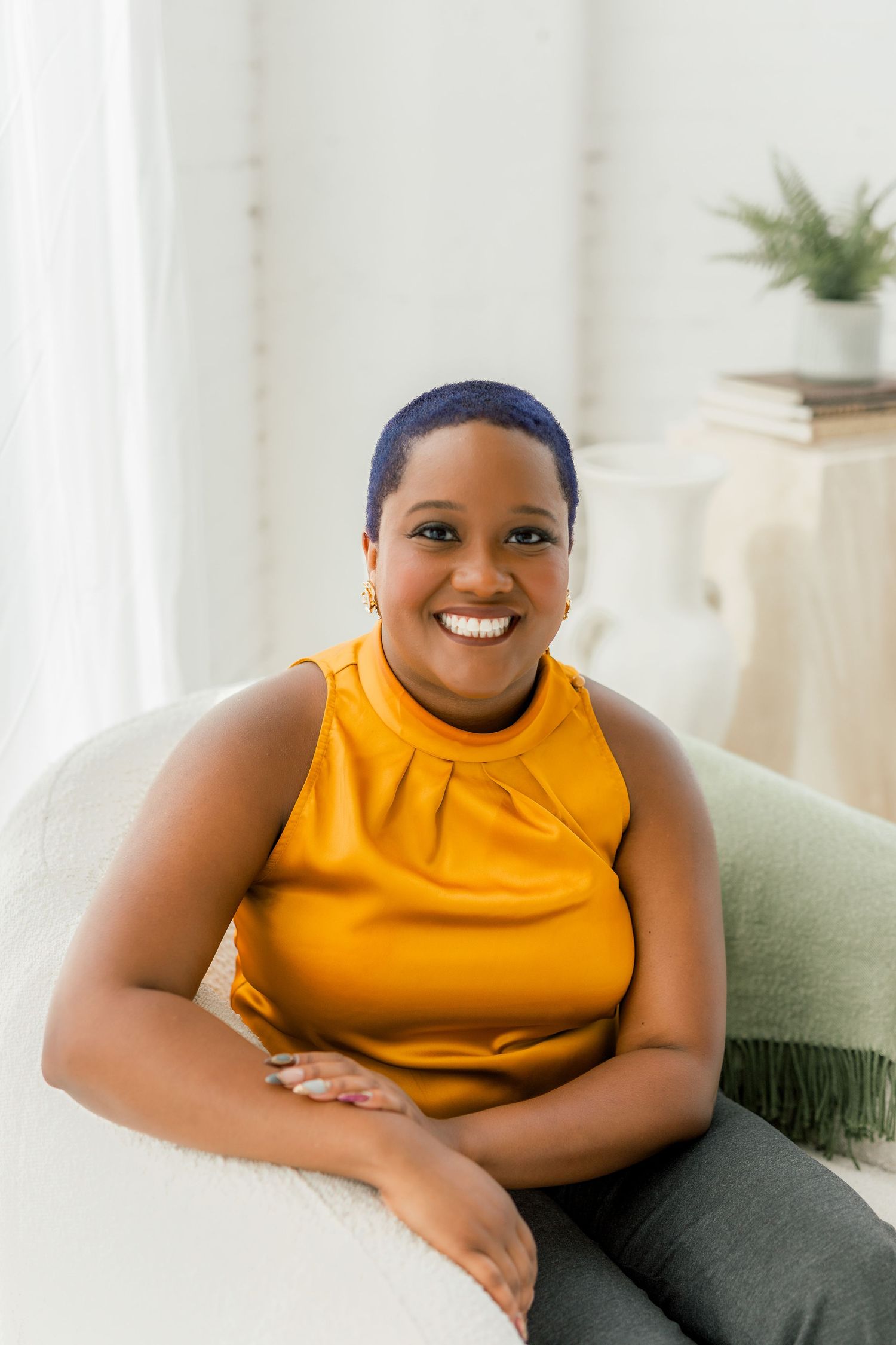 Cheerful portrait in mustard yellow sleeveless top seated on light couch.