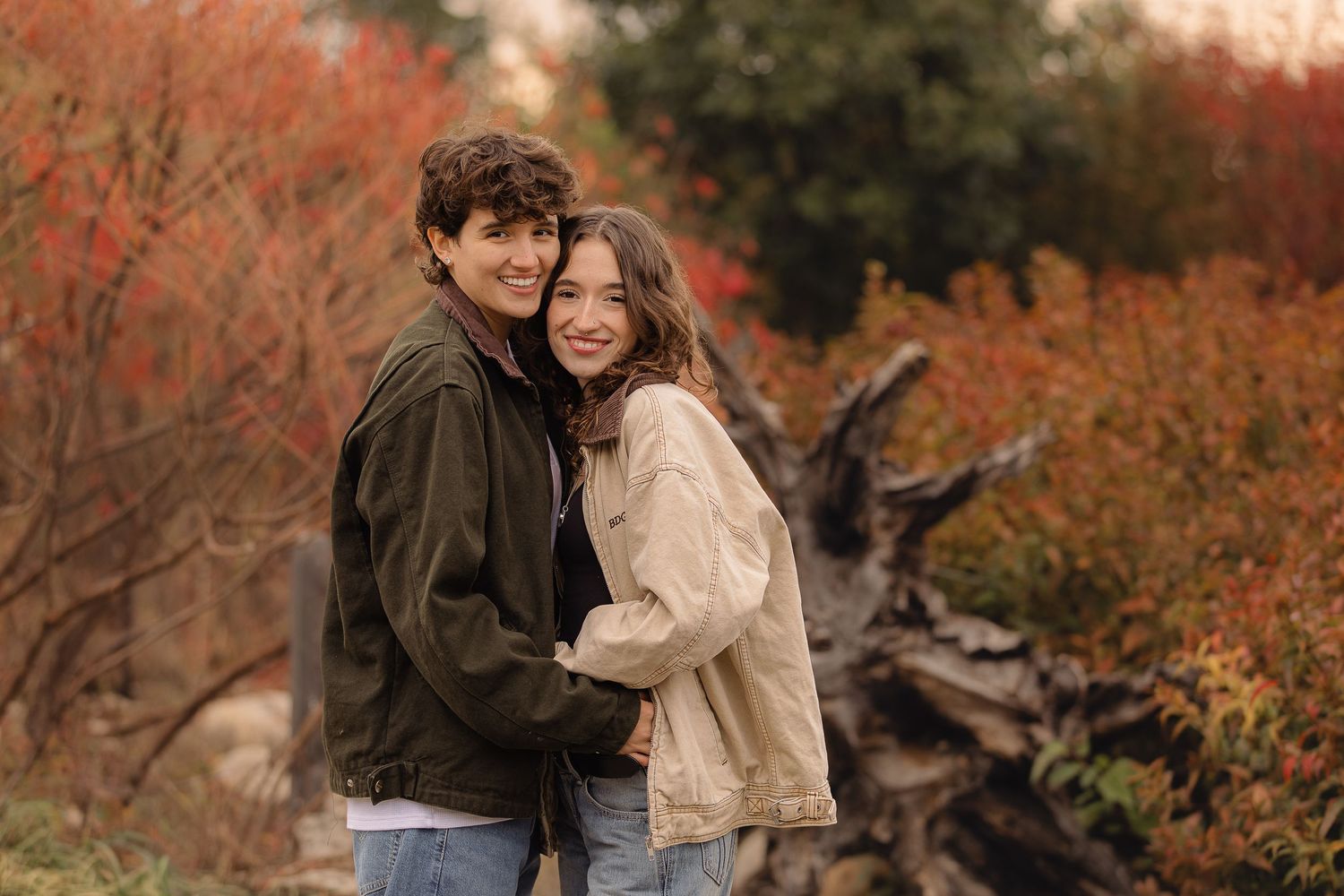 A couple embraces on a nature trail surrounded by warm fall colors and sunlit trees.