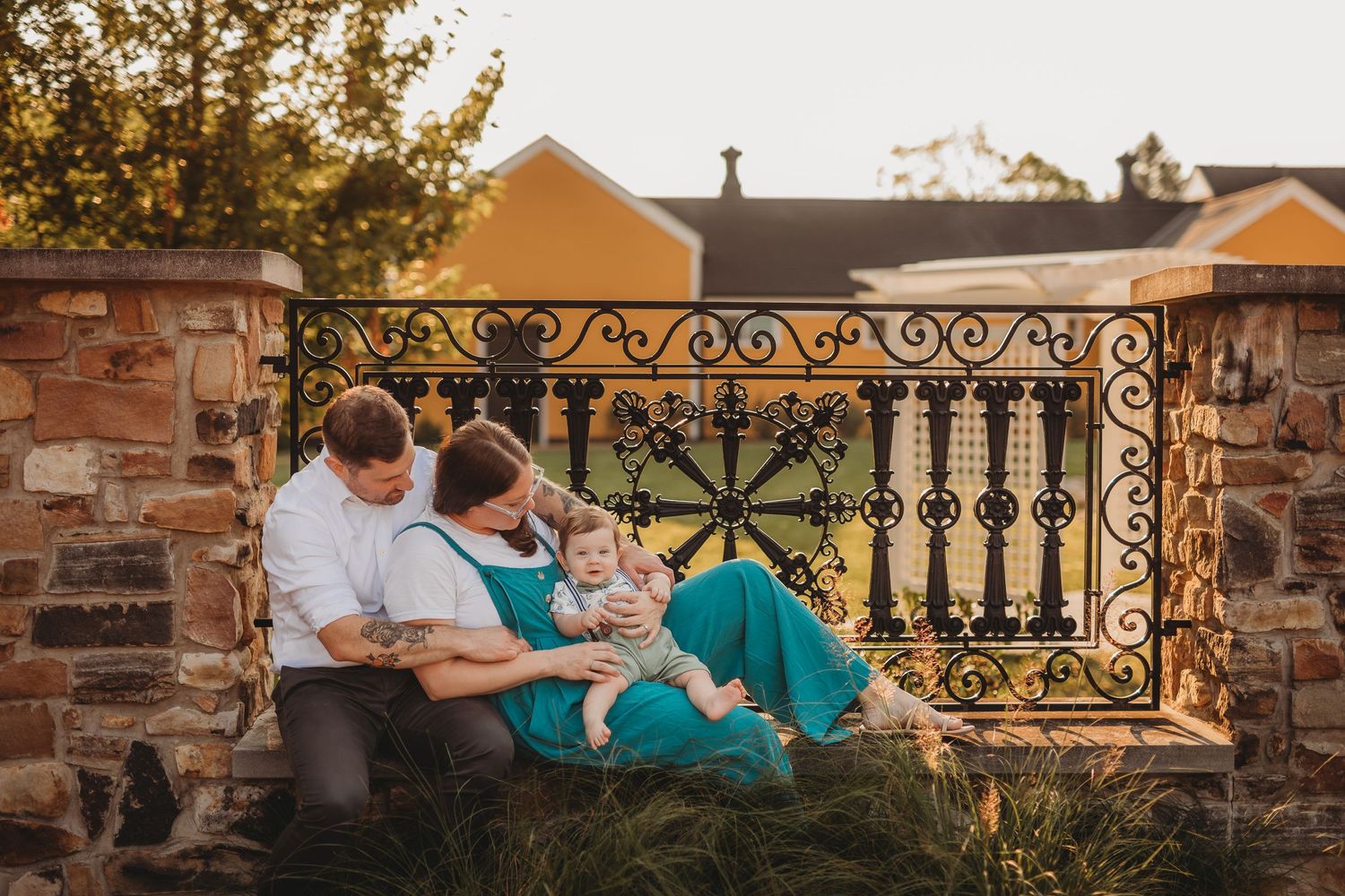 Family relaxing together on ornate stone wall during golden hour.