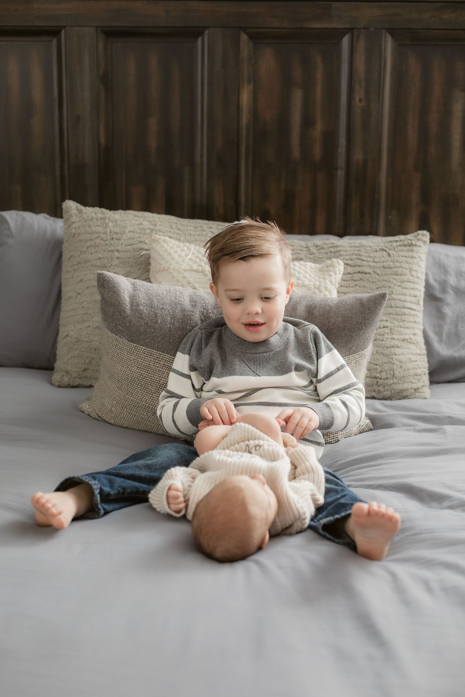 Baby in striped outfit playing on grey bedding.