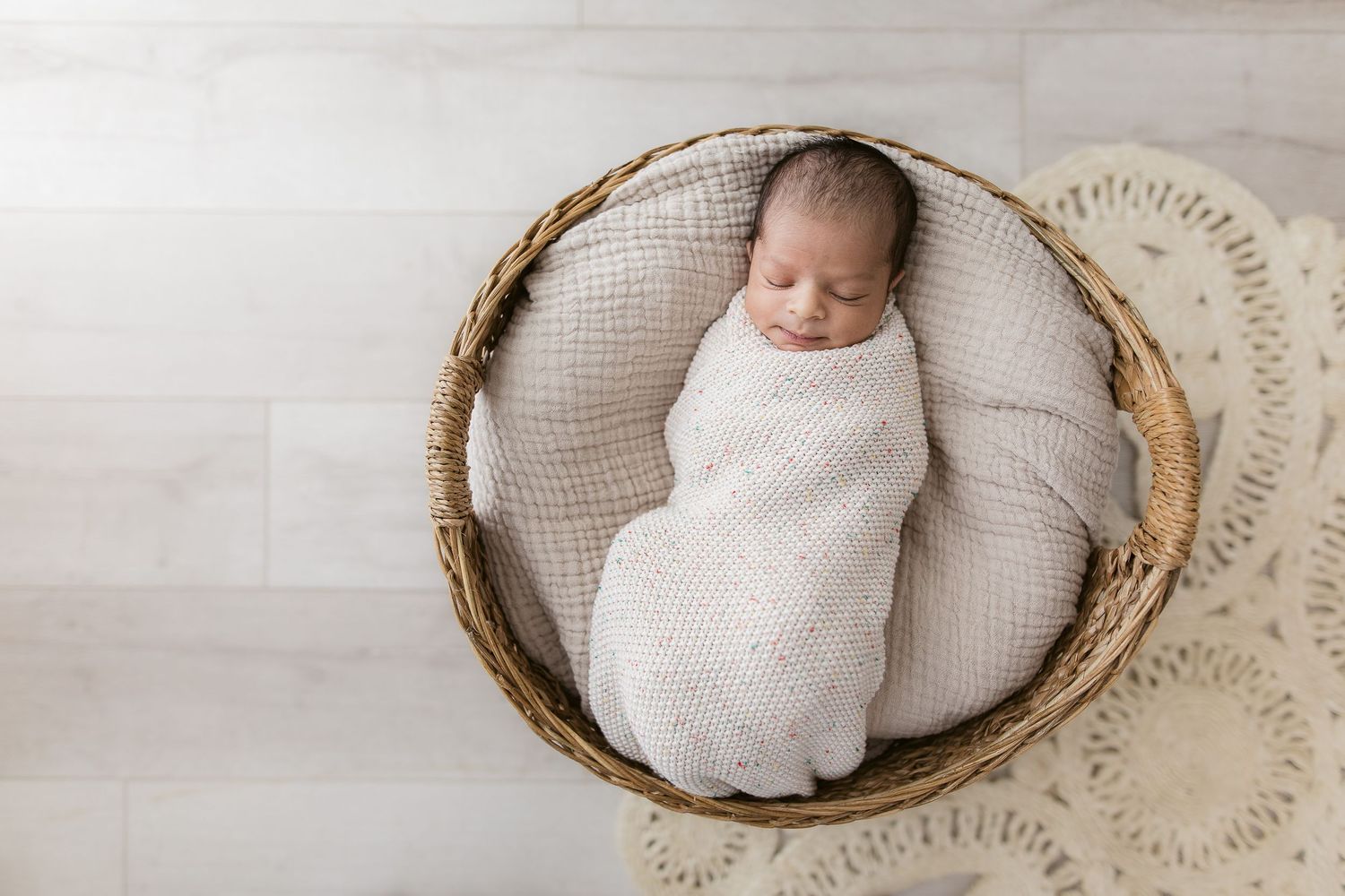 Sleeping newborn swaddled in white wrap inside round woven basket.