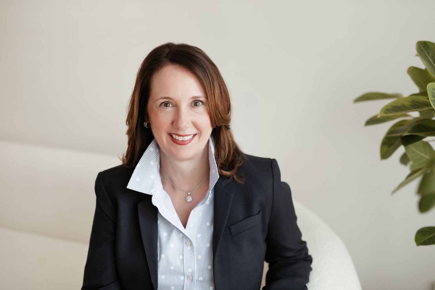 Professional woman in black blazer smiling confidently in a bright modern office setting.