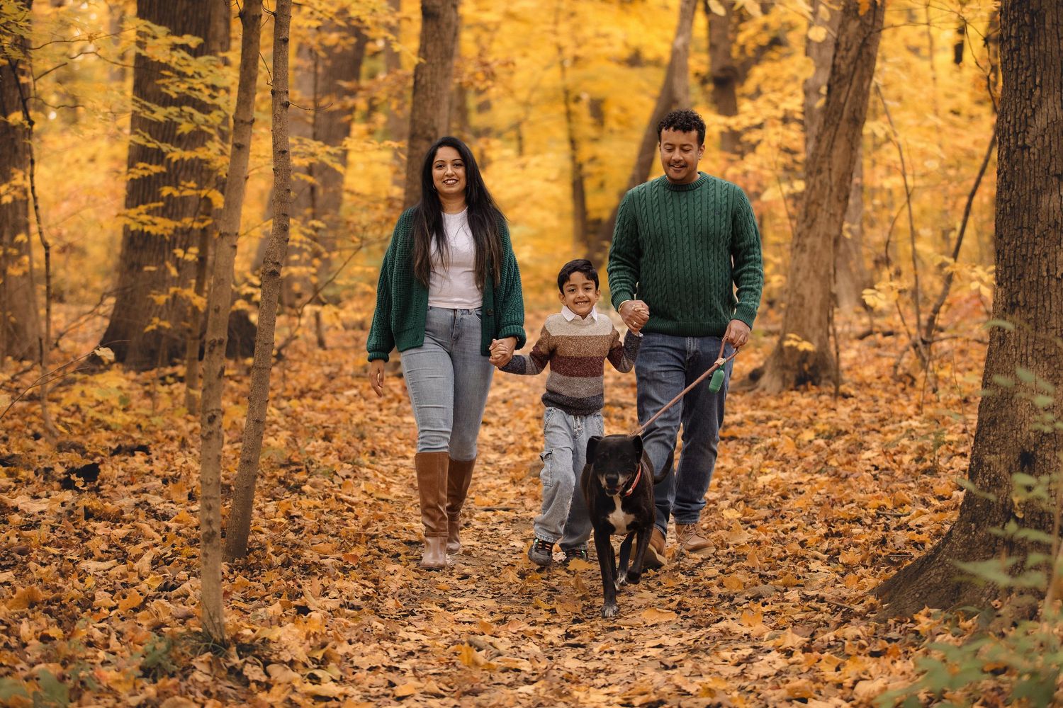 A family enjoys an autumn walk together through a forest covered in fallen leaves.