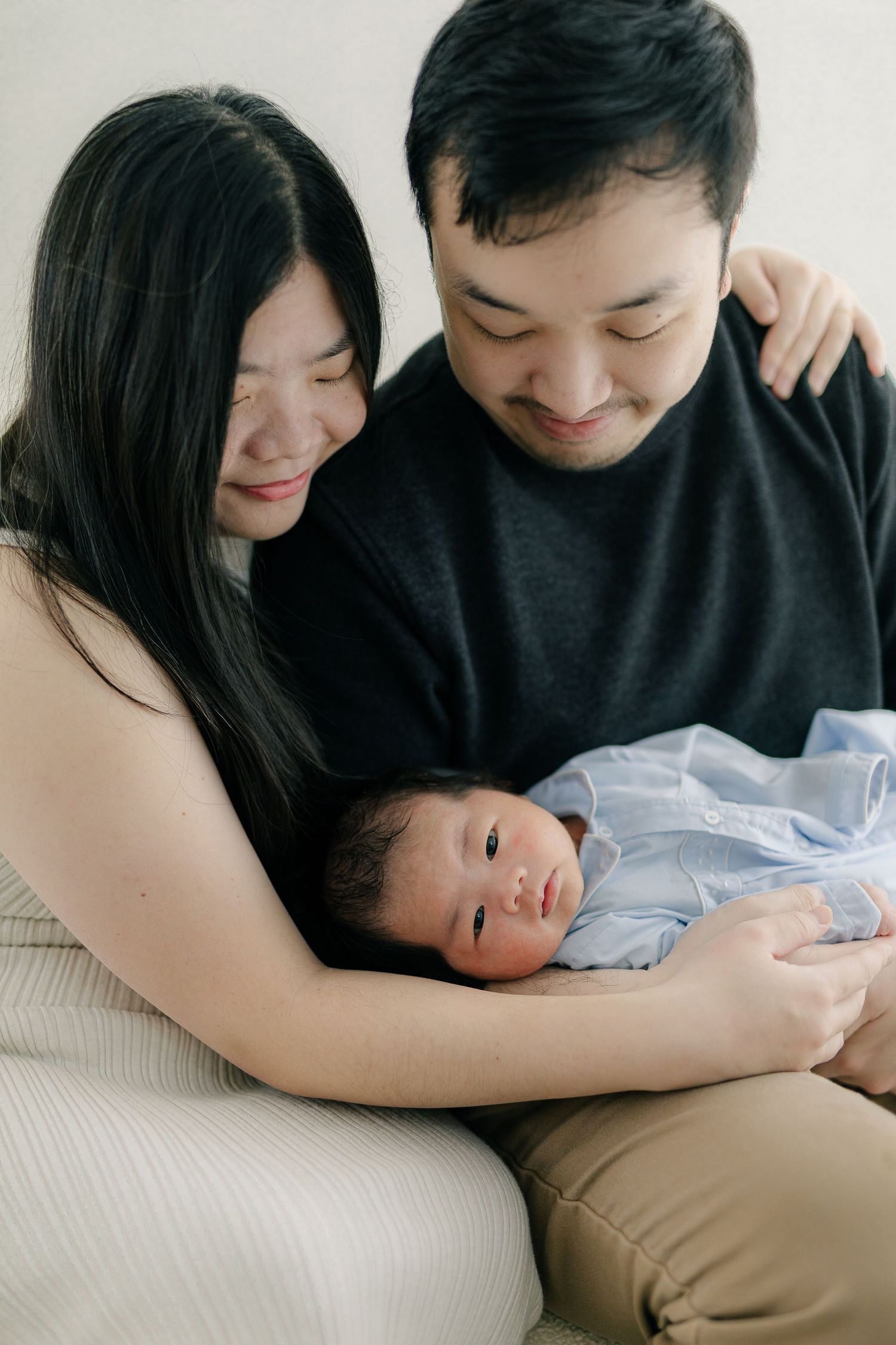 Intimate newborn photography session with parents in black sweaters on white background.