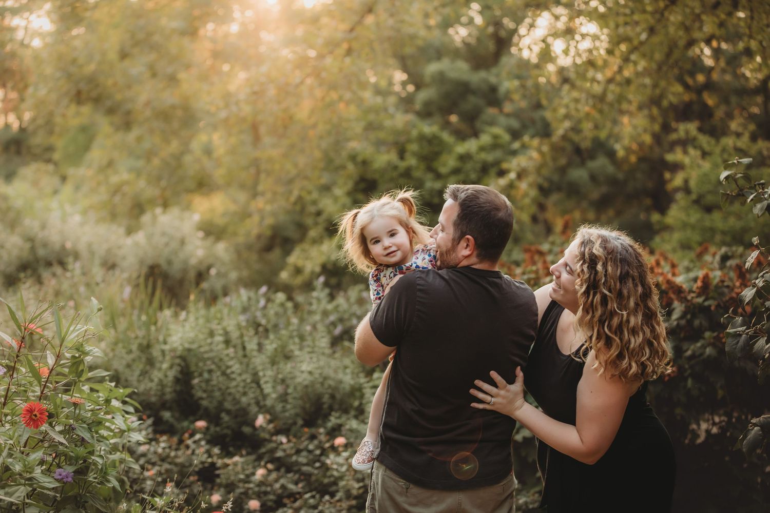 A family shares a joyful moment together outdoors during golden hour in a natural garden setting.