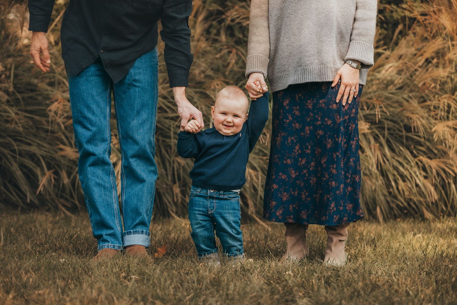 A family wearing casual clothing stands together in tall golden grass during sunset.