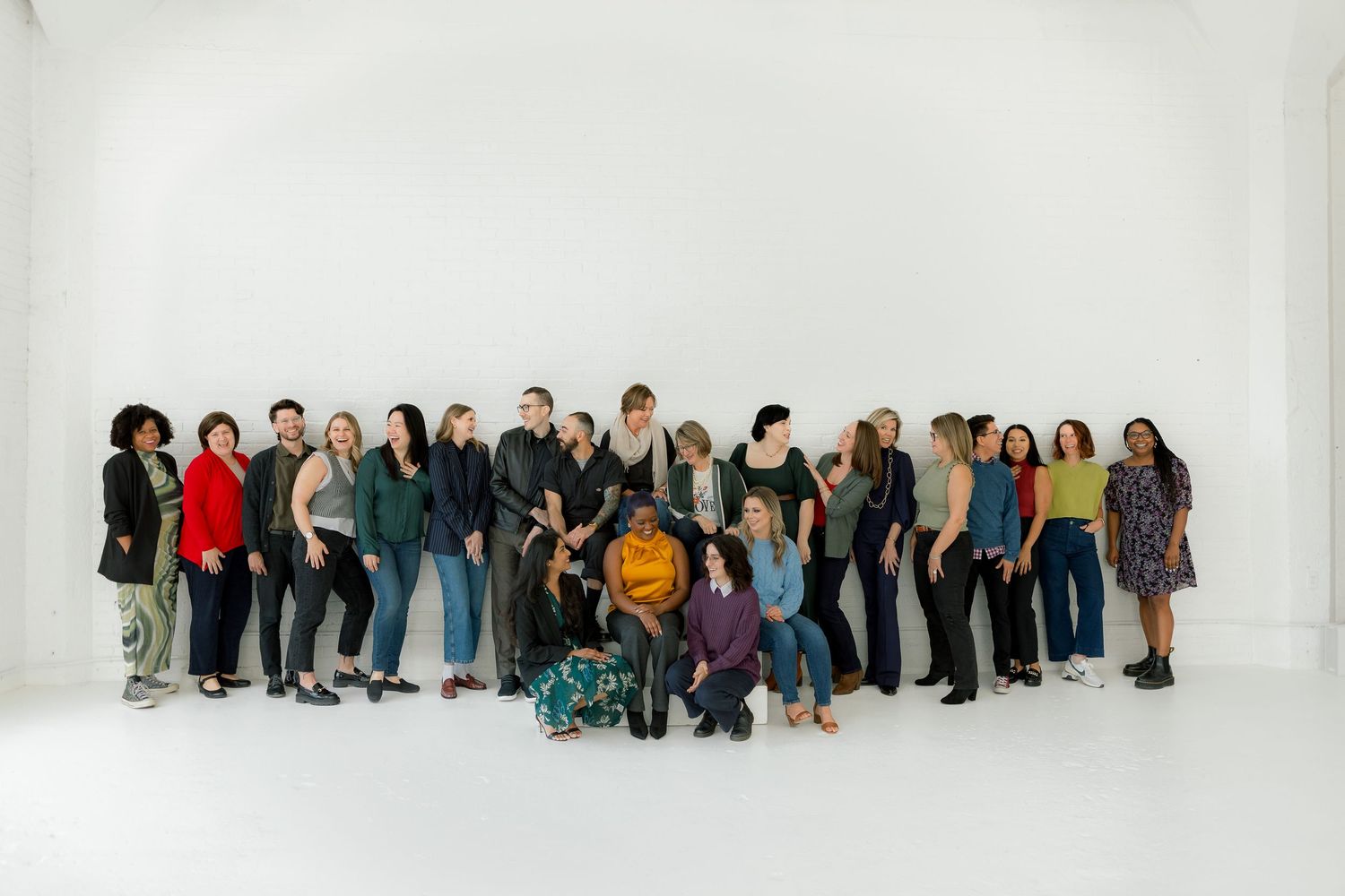 Large diverse group of people posing together against white background in casual business attire.