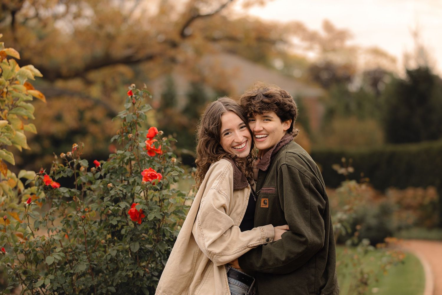 Couple embracing among red rose bushes in an autumn garden setting.