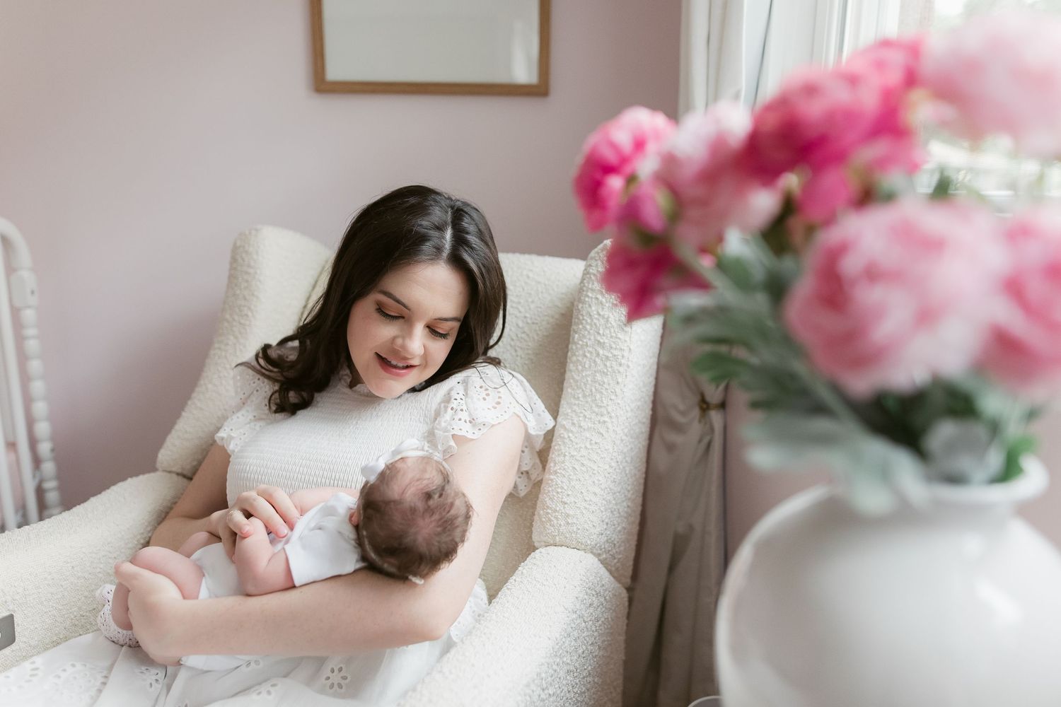 A tender moment captured in a bright white nursery with pink floral accents and soft natural lighting.