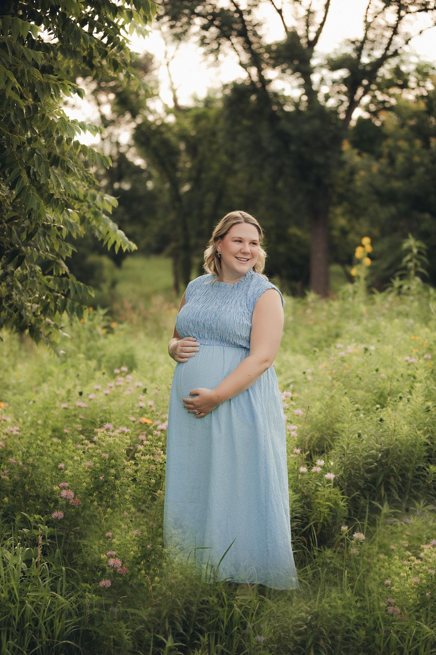 Woman in light blue dress poses in wildflower field during golden hour.