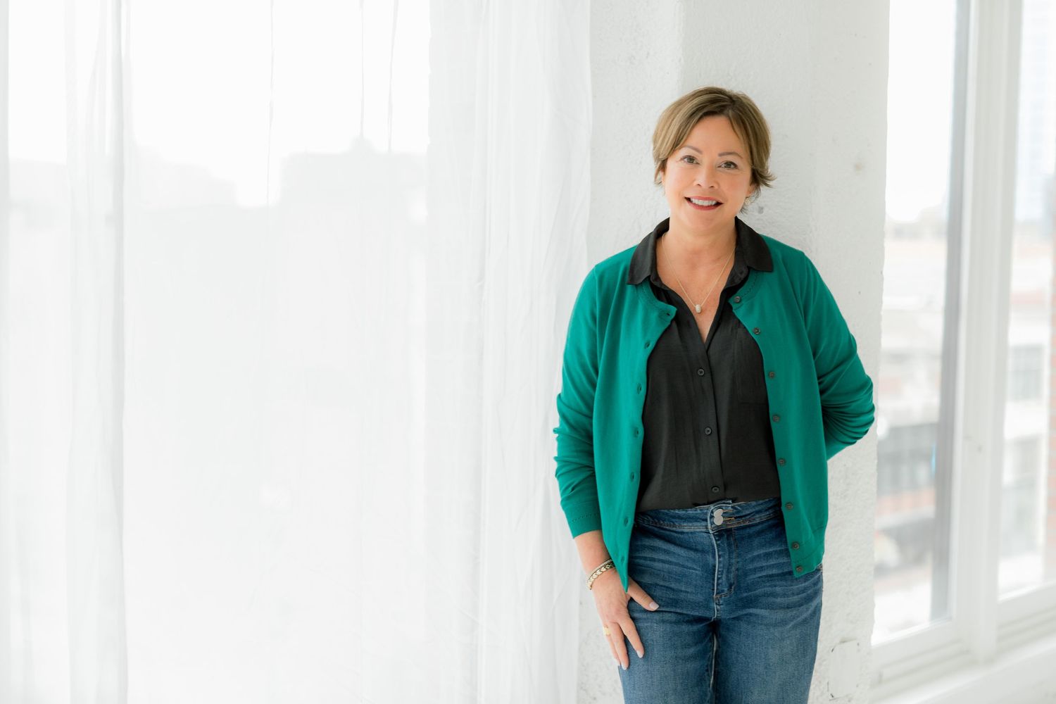 Professional wearing a green blazer and black top poses in a bright studio setting.