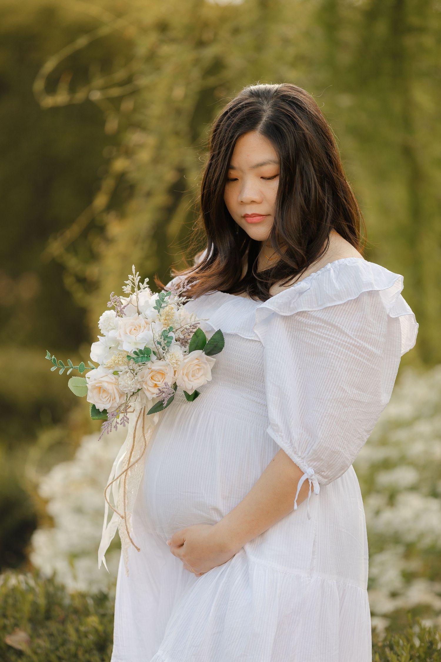 A maternity photo series featuring a woman in a white dress holding a delicate floral bouquet.