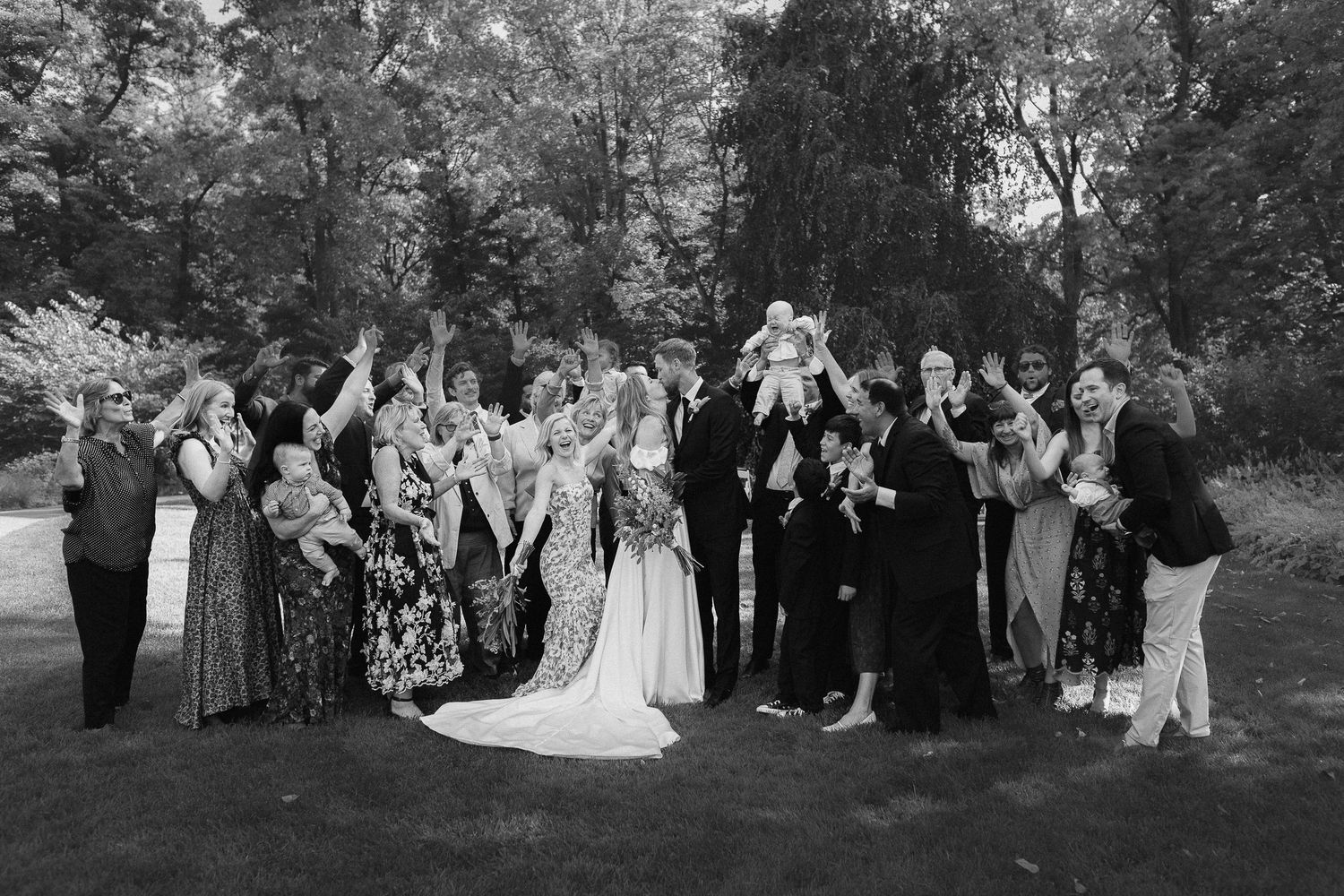 Black and white wedding photo of large group celebrating outdoors.
