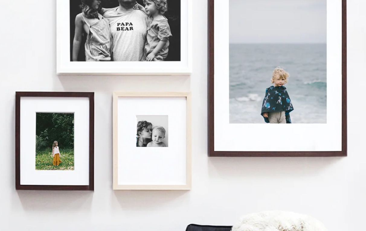 A gallery wall display featuring four framed family photos in various sizes and frame colors on a white wall.